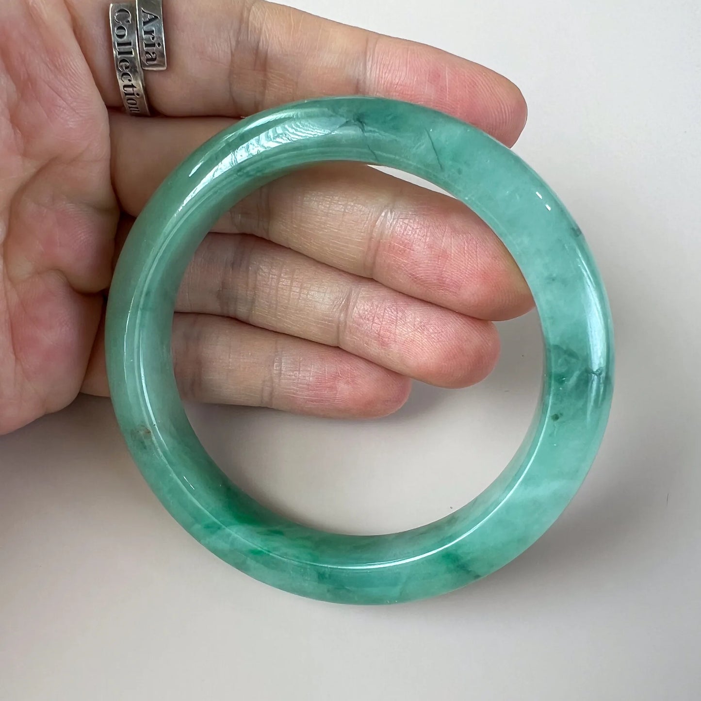 Close hand-held view of translucent green jade bangle with natural inclusions