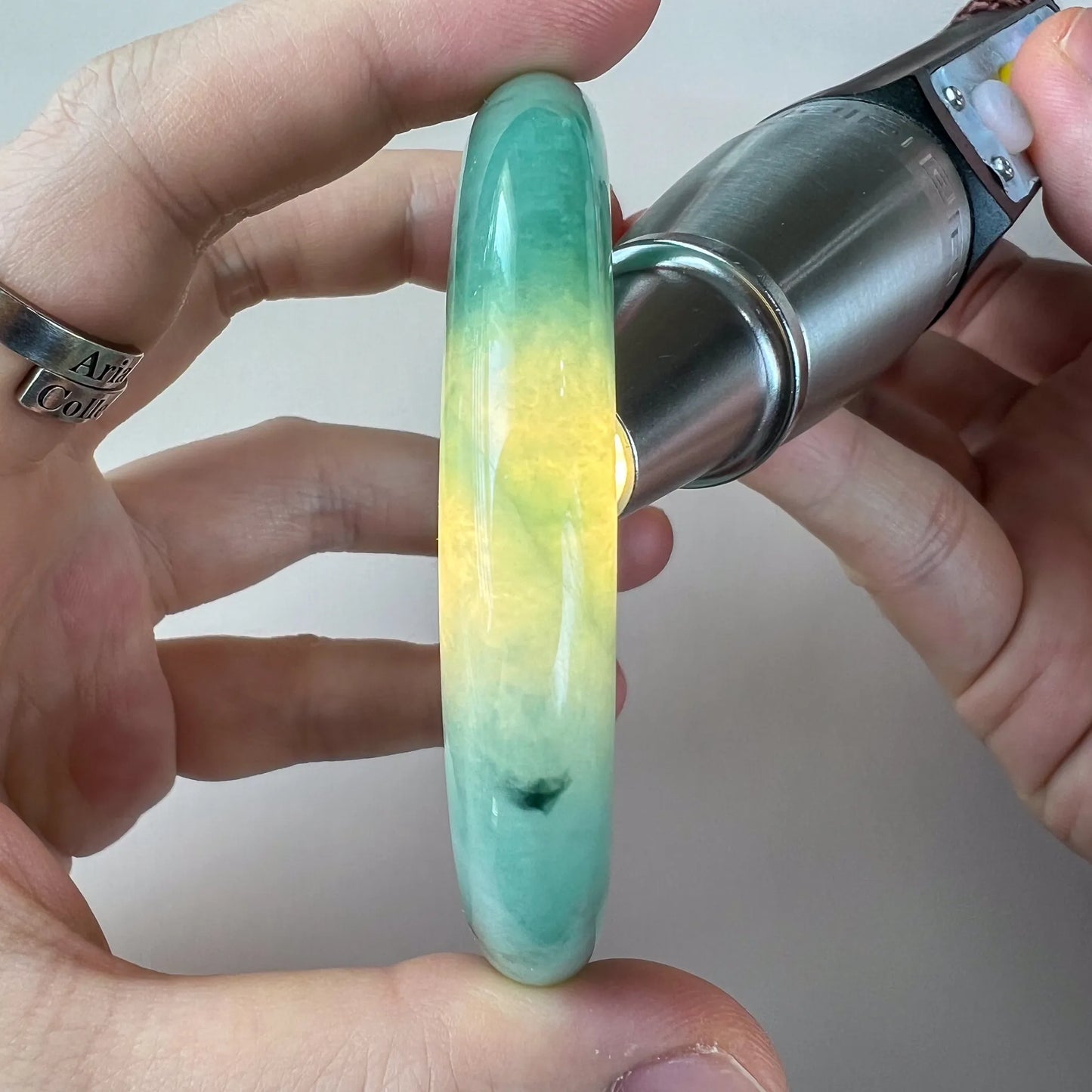 Side profile of glossy green-to-yellow jade bangle held in hand