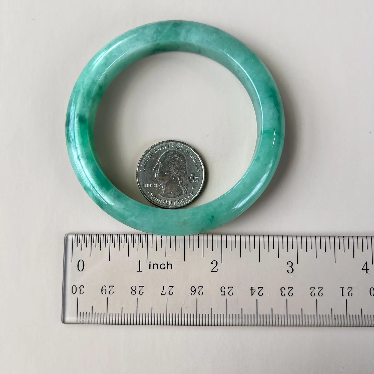Light green-blue jadeite bangle shown beside a ruler and quarter for size reference
