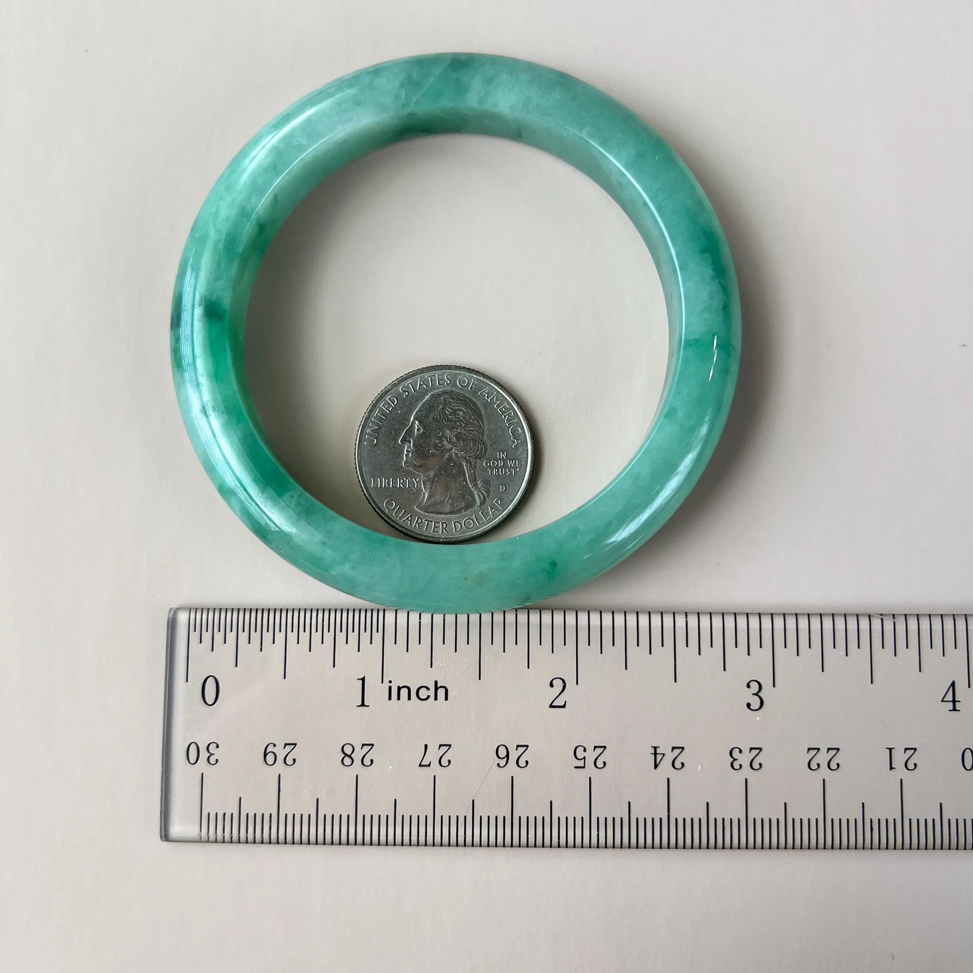 Light green-blue jadeite bangle shown beside a ruler and quarter for size reference