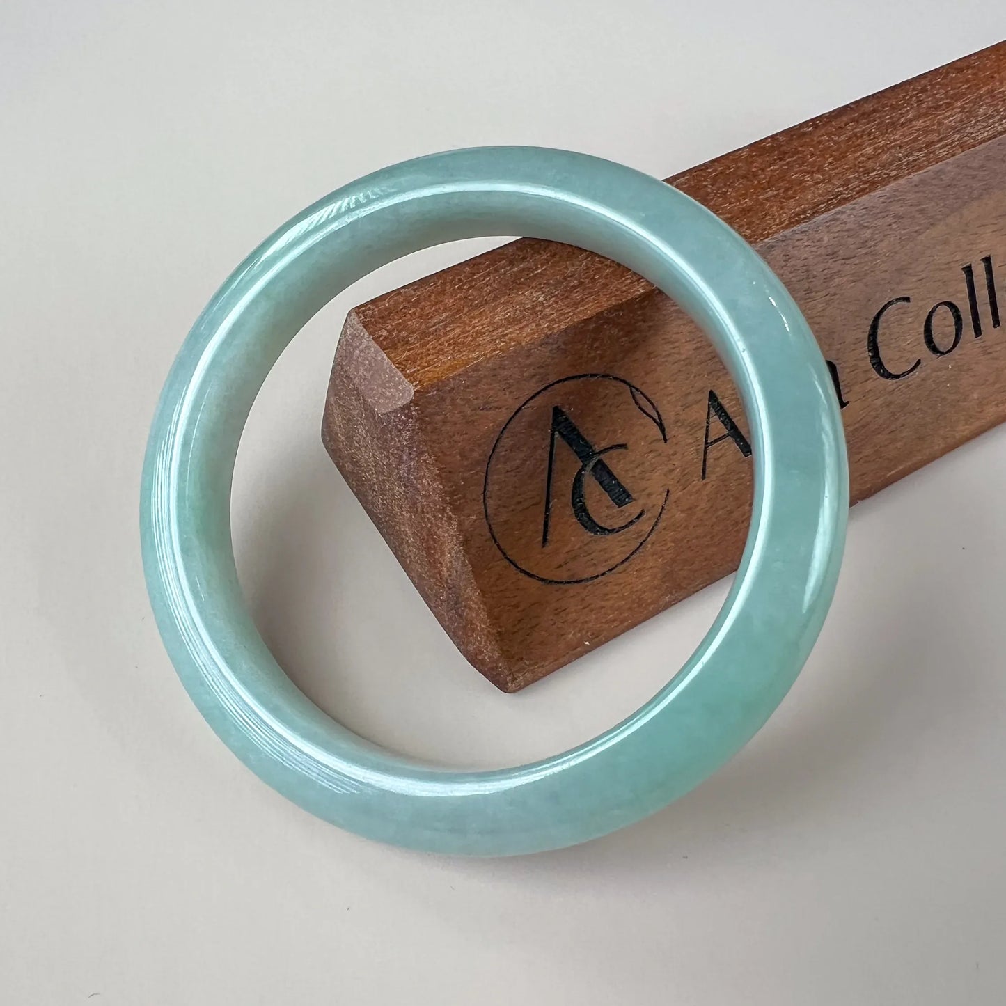 Glossy pale jade bangle shown at a slight angle on a white background with wooden stand