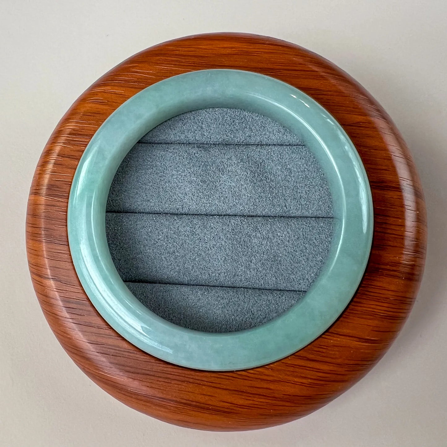 Top view of polished jade bangle in a wooden display box with gray velvet lining
