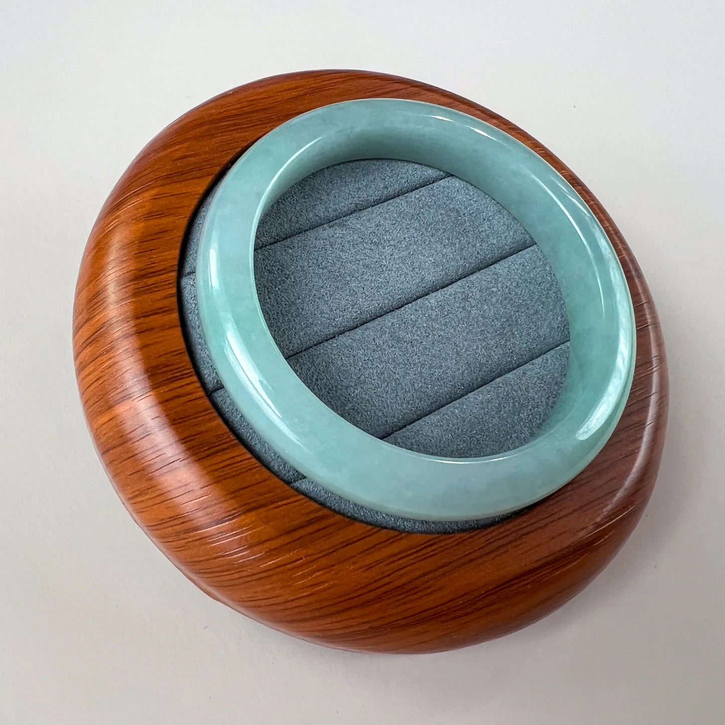 Angled view of smooth jade bangle in a round wooden presentation box with velvet interior