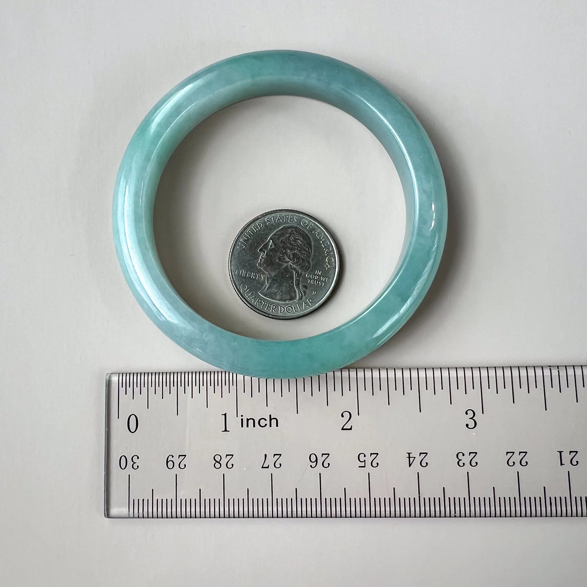 Light green-blue jadeite bangle shown beside a ruler and quarter for size and scale