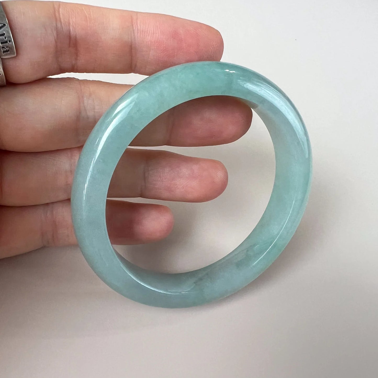 Close handheld view of smooth round jade bangle with glossy finish and pale green tone