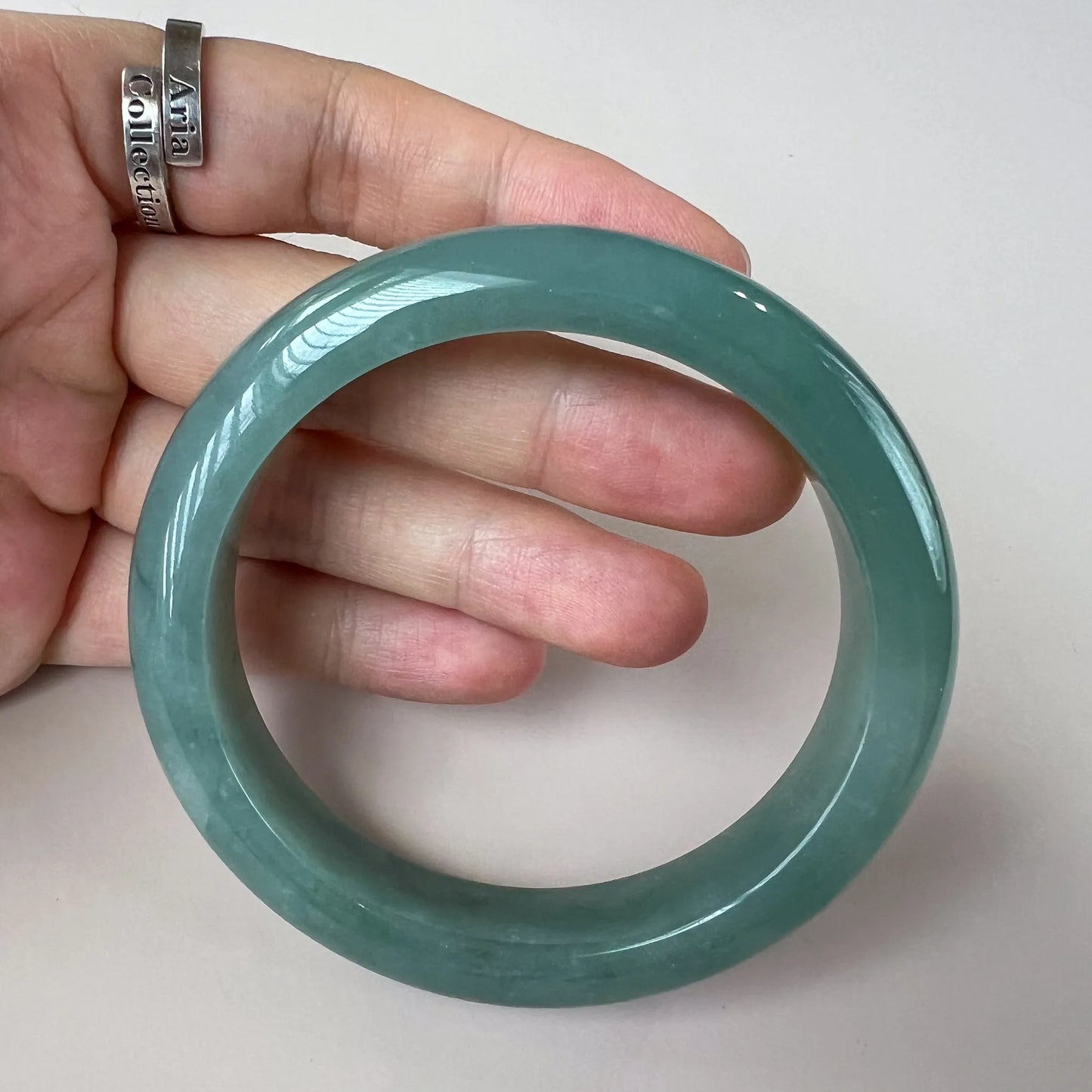 Handheld view of smooth green jade bangle, glossy polished finish