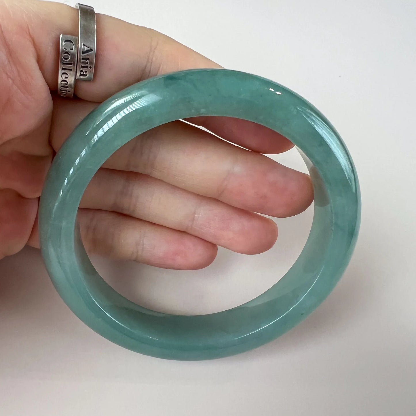 Close handheld view of rounded jade bangle with translucent green finish