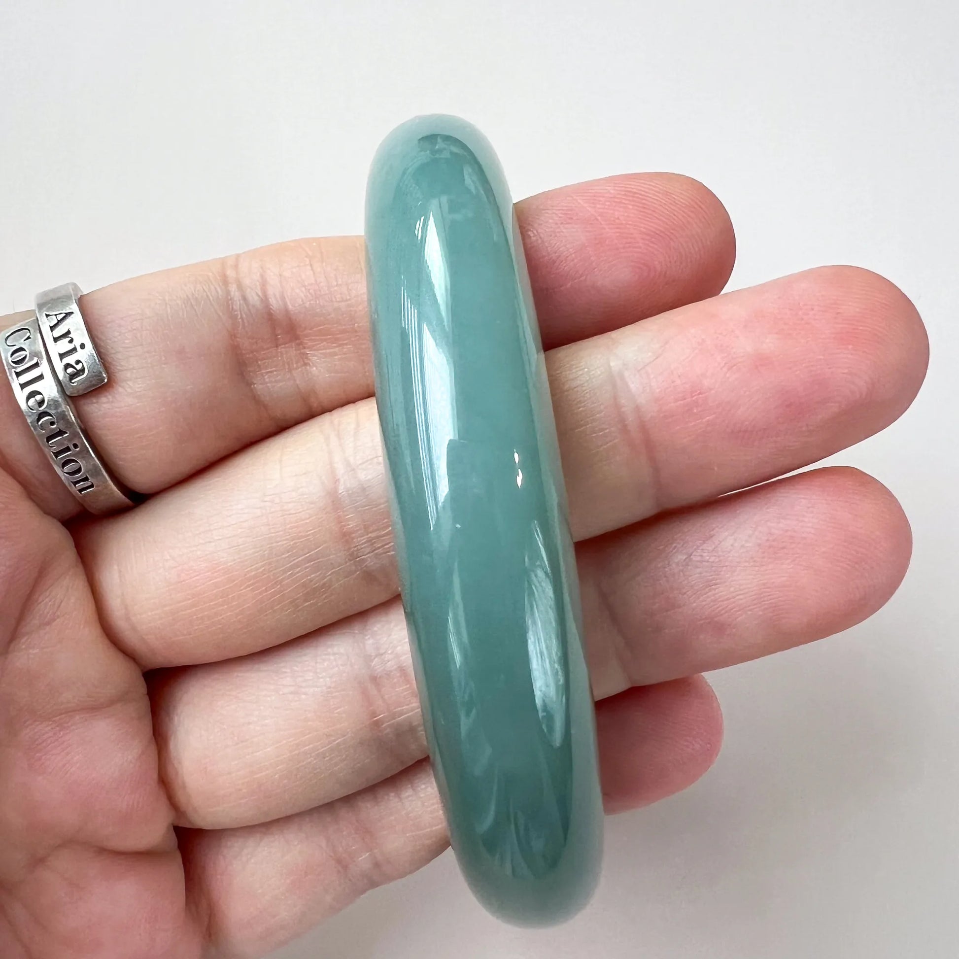 Side profile of thick polished green jade bangle held in hand