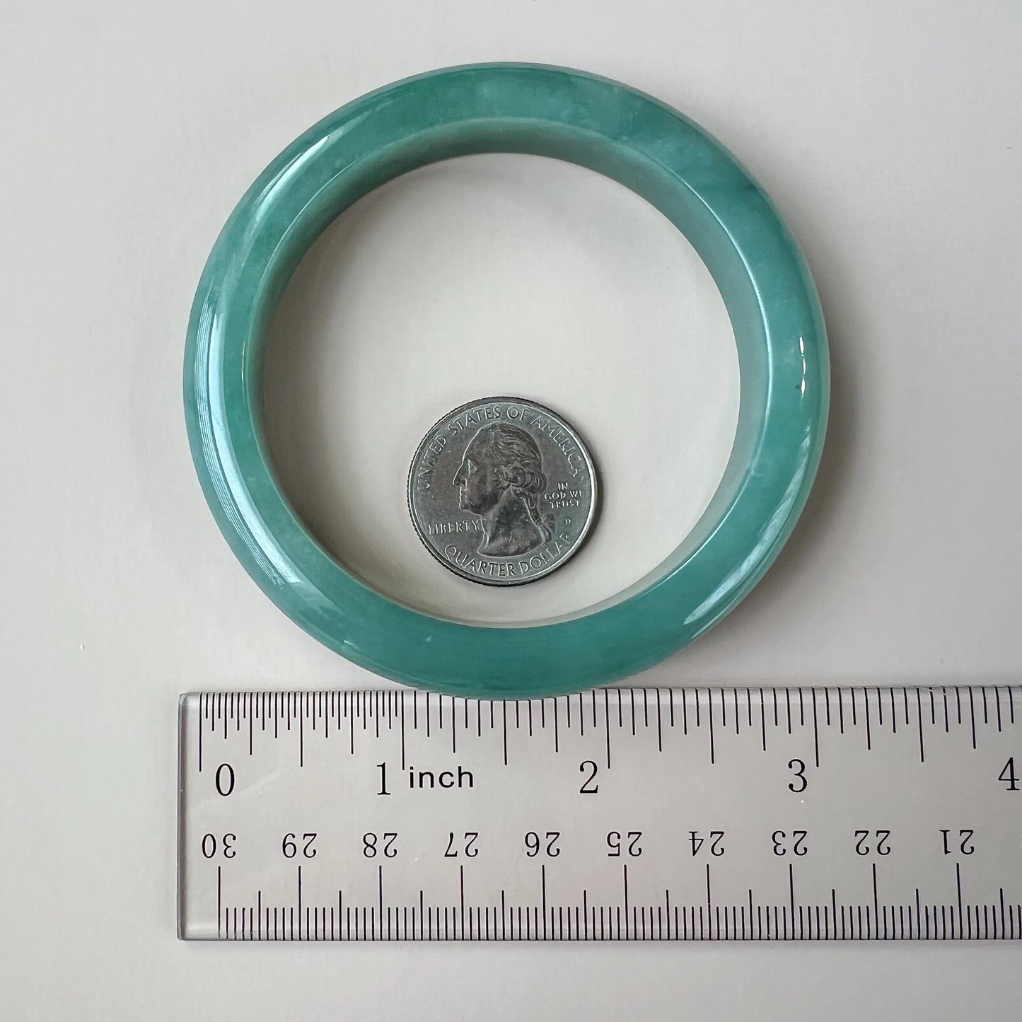 Light green-blue jadeite bangle shown beside a ruler and quarter for size reference