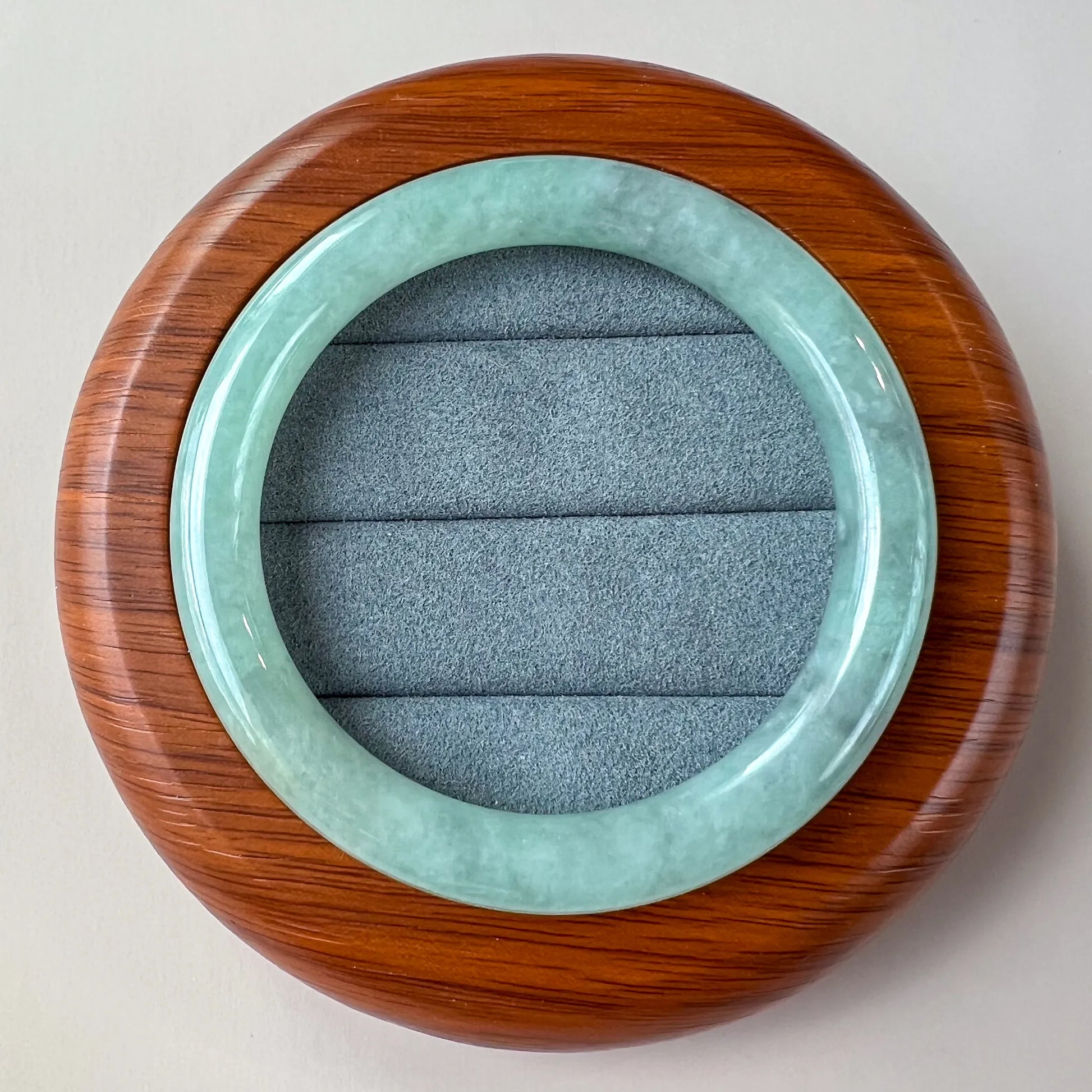 Top-down view of glossy light green jade bangle in round wood case