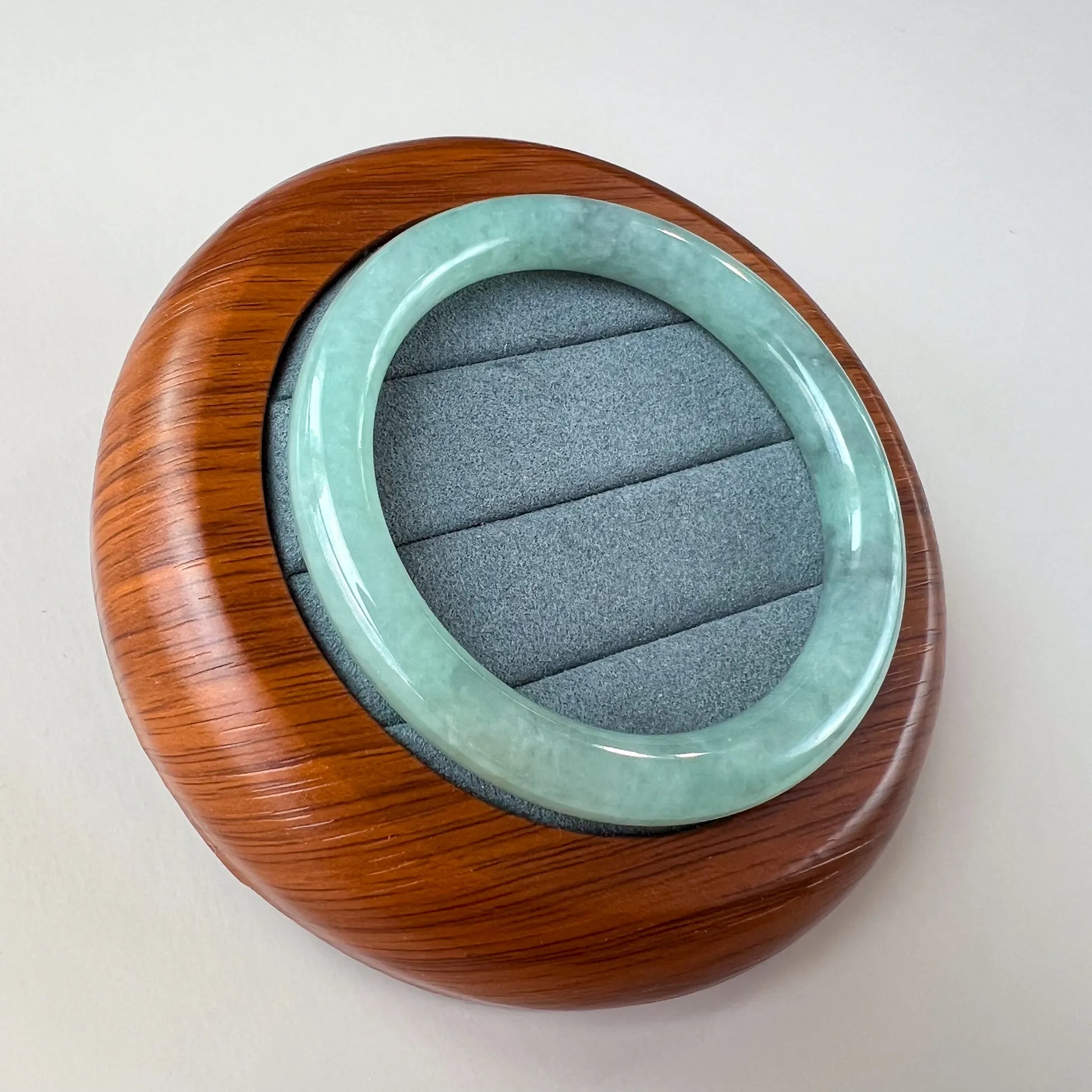 Angled view of smooth jade bangle in carved wooden display case