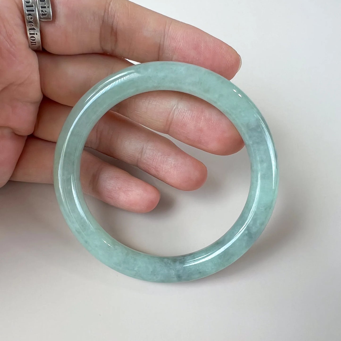 Handheld front view of translucent green jade bangle with polished finish