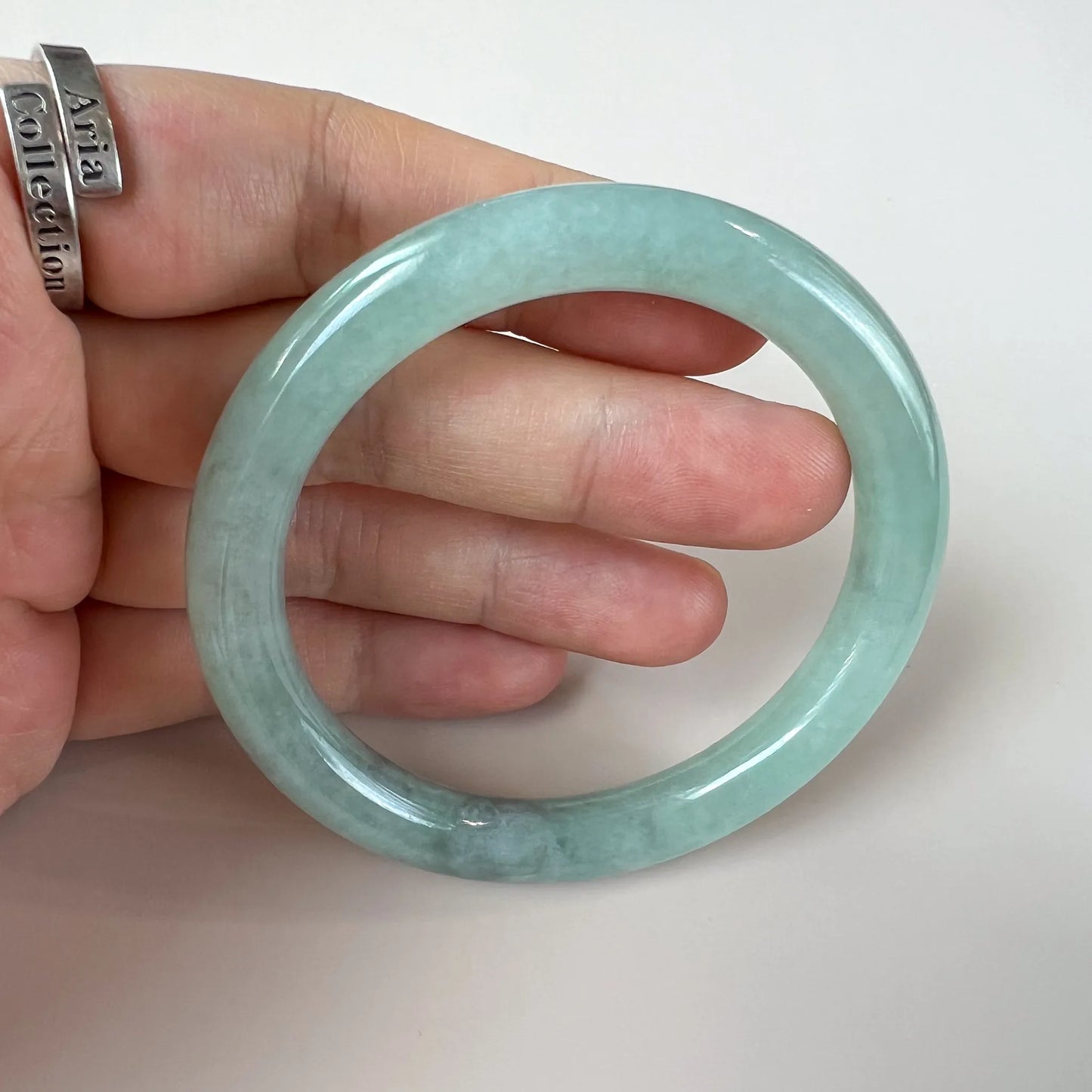 Side view of slim polished jade bangle shown on hand for scale