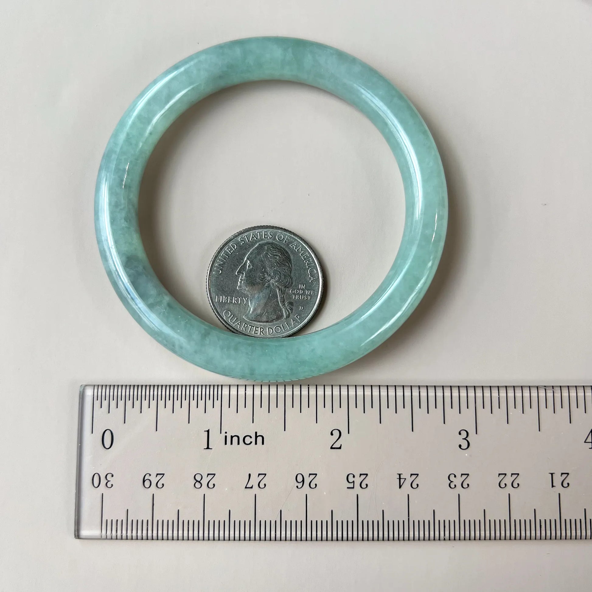 Green-blue jadeite bangle shown beside a ruler and quarter for scale