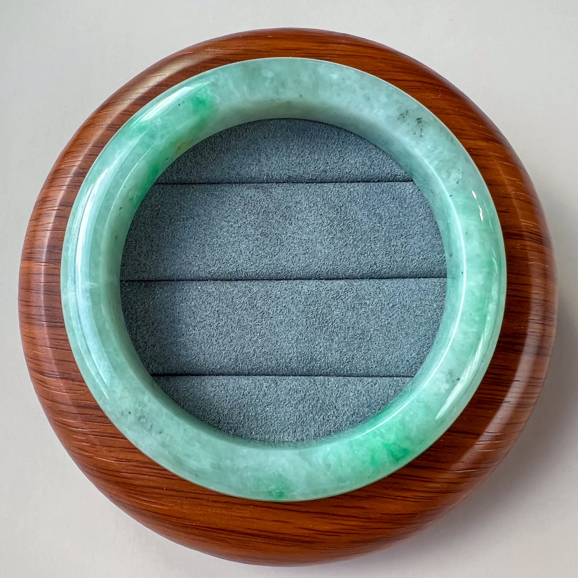 Jade bangle displayed on round wooden stand with gray padded insert, top-down view