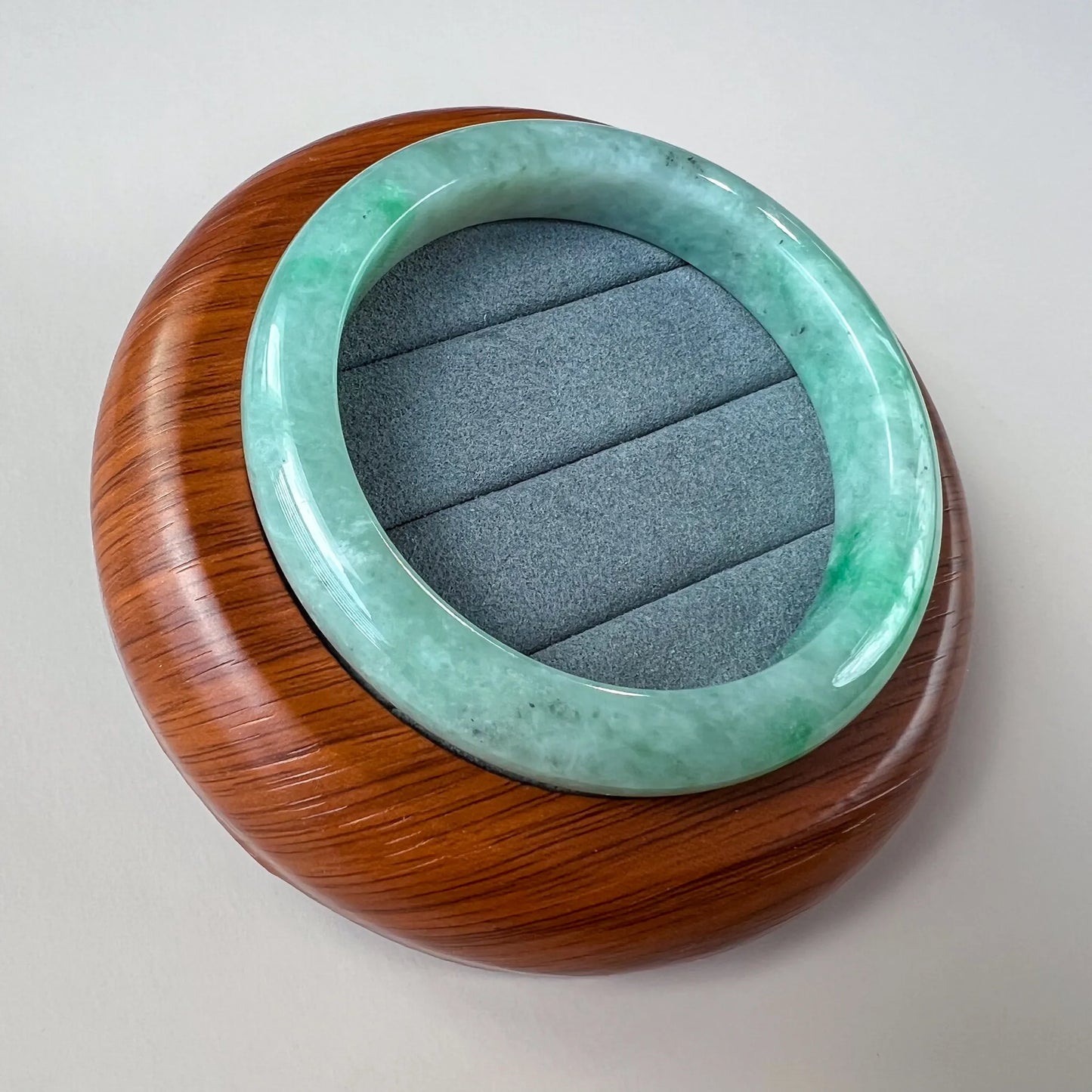 Angled view of glossy green jade bangle resting on wood display stand