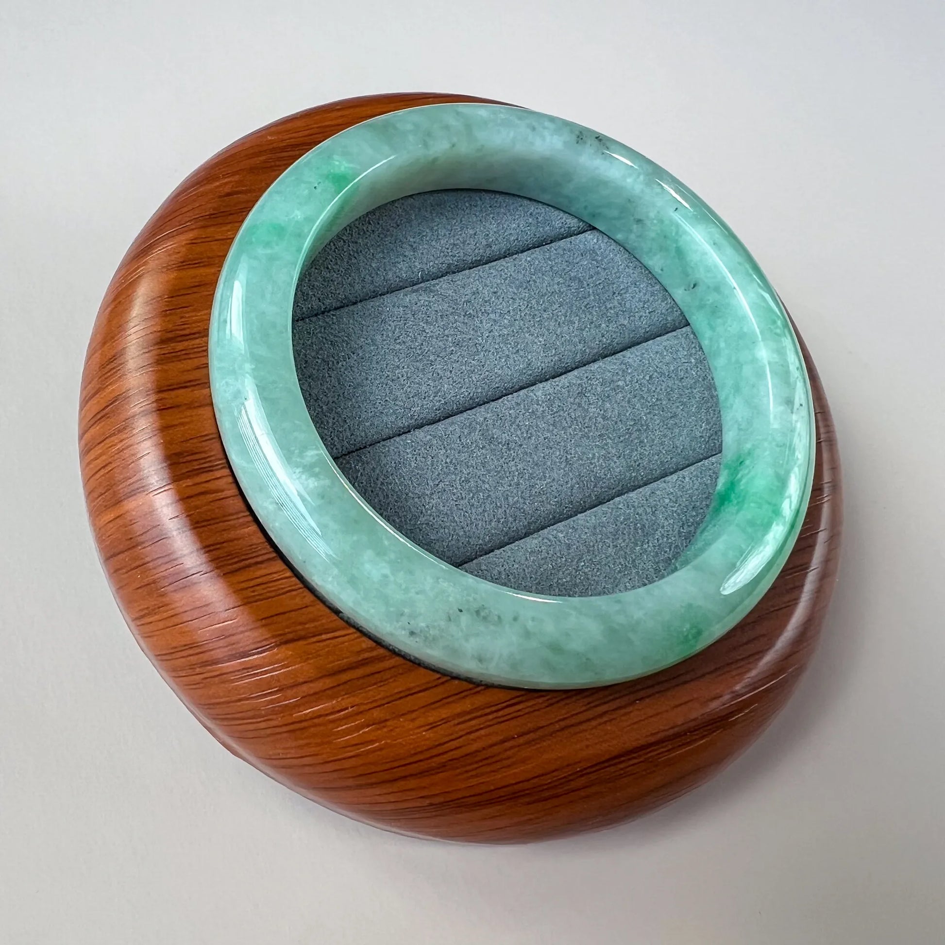 Angled view of glossy green jade bangle resting on wood display stand