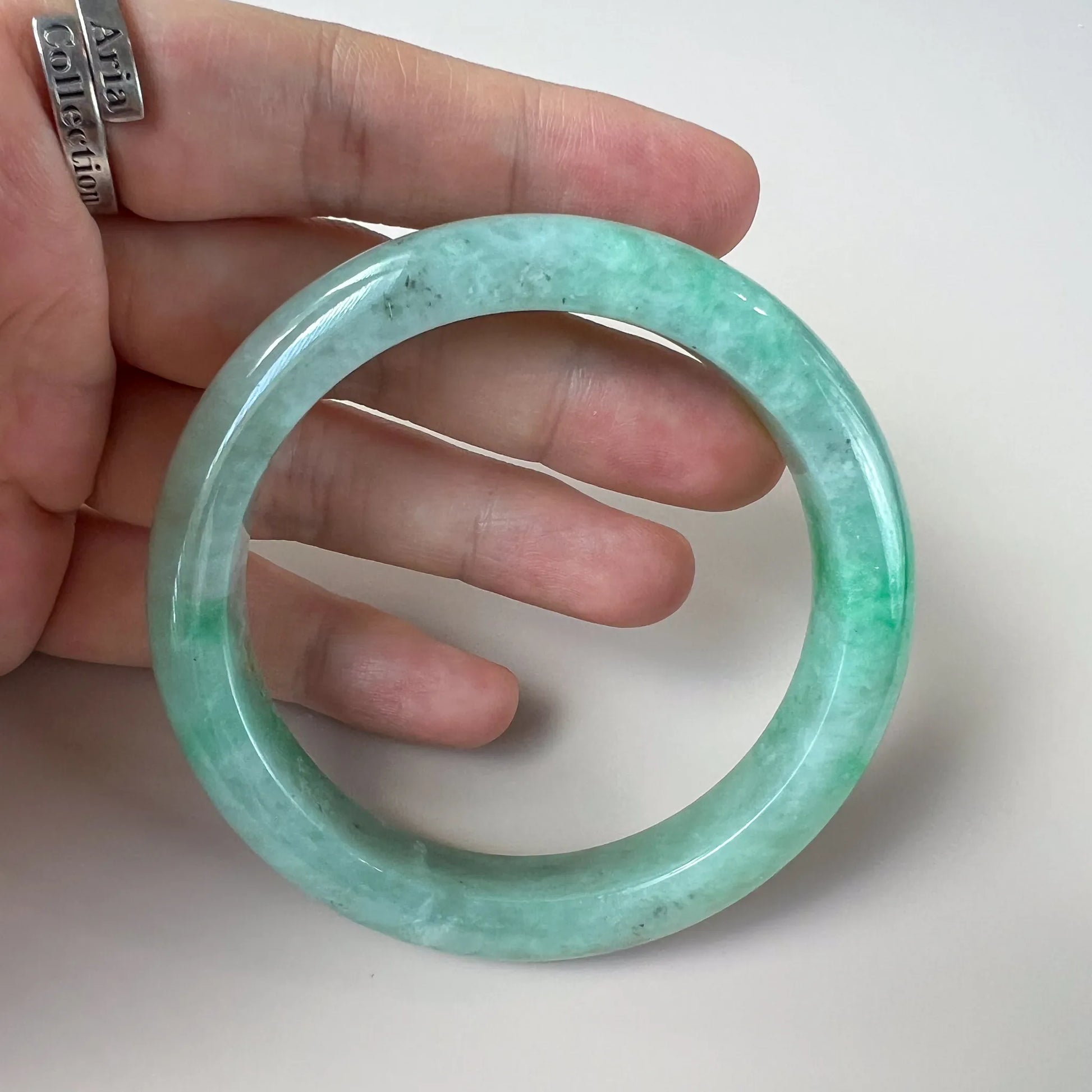 Handheld view of translucent green jade bangle showing polished finish and natural inclusions