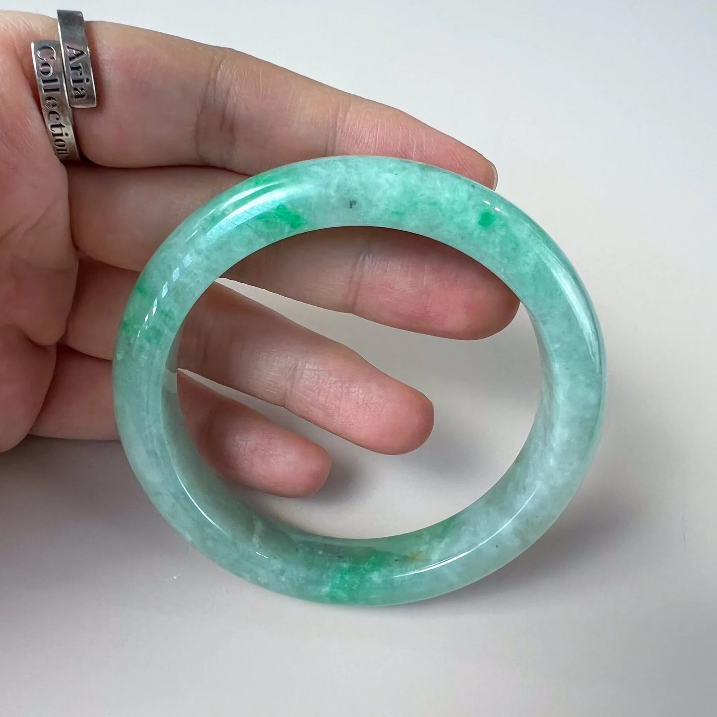 Handheld close-up of green jade bangle with glossy surface and mottled color variations