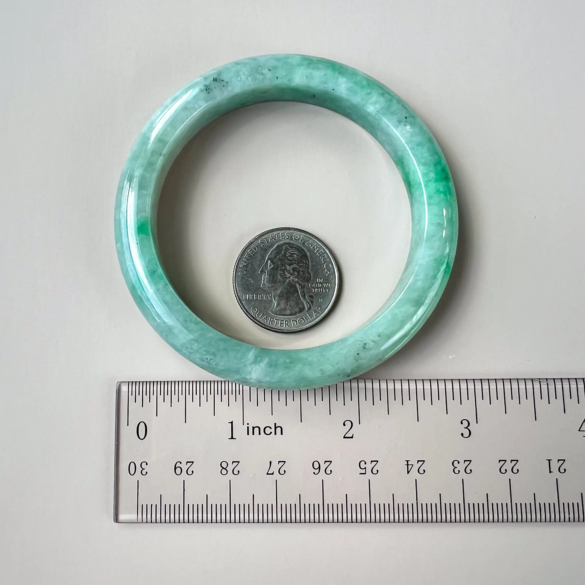 Mint-green jadeite bangle shown beside a ruler and quarter for size reference