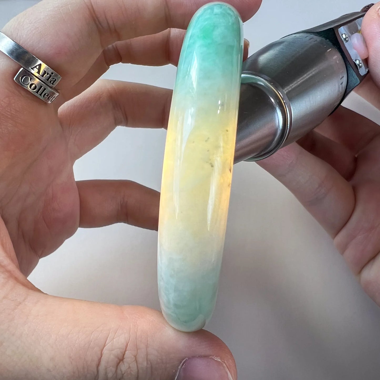 Side profile of jade bangle held in hand under magnification light, showing thick rounded shape