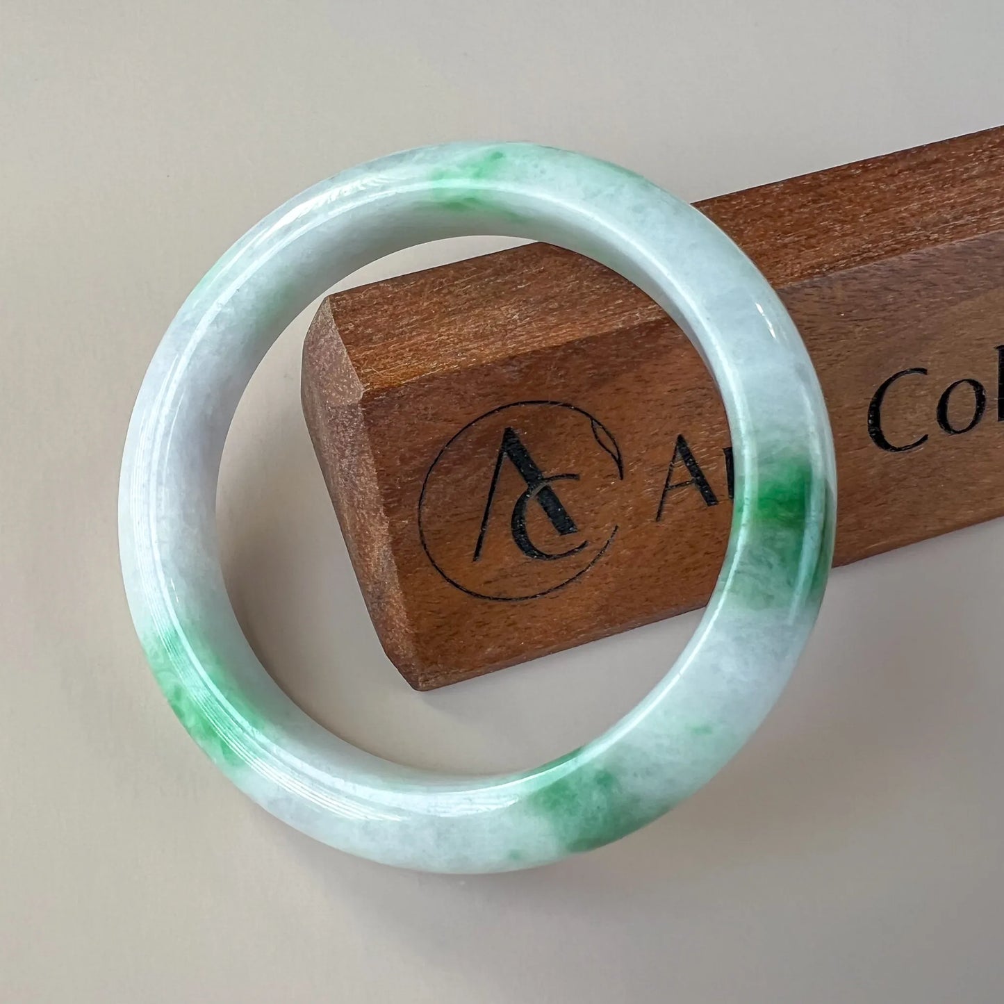 Front view of polished jade bangle with green marbling on a wooden stand