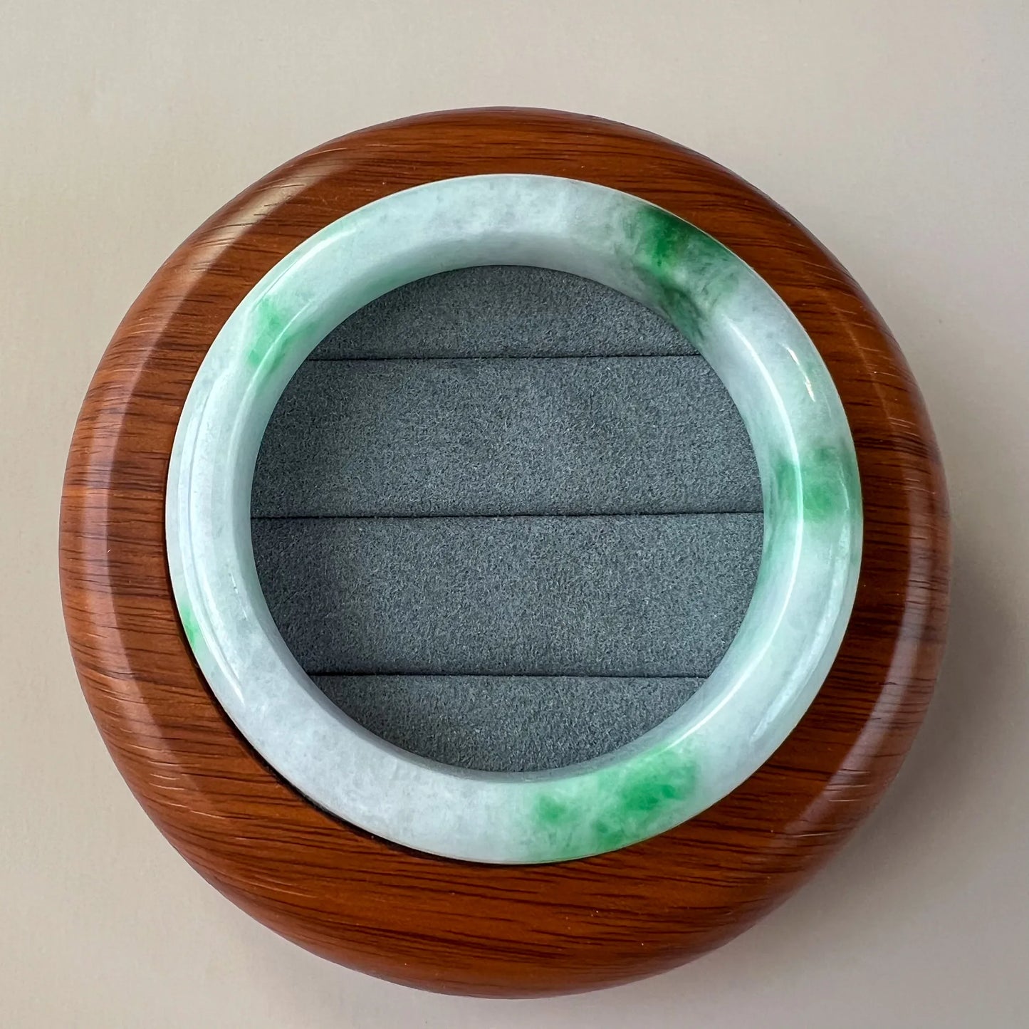 Jade bangle displayed on round wooden cushion, showing smooth glossy finish