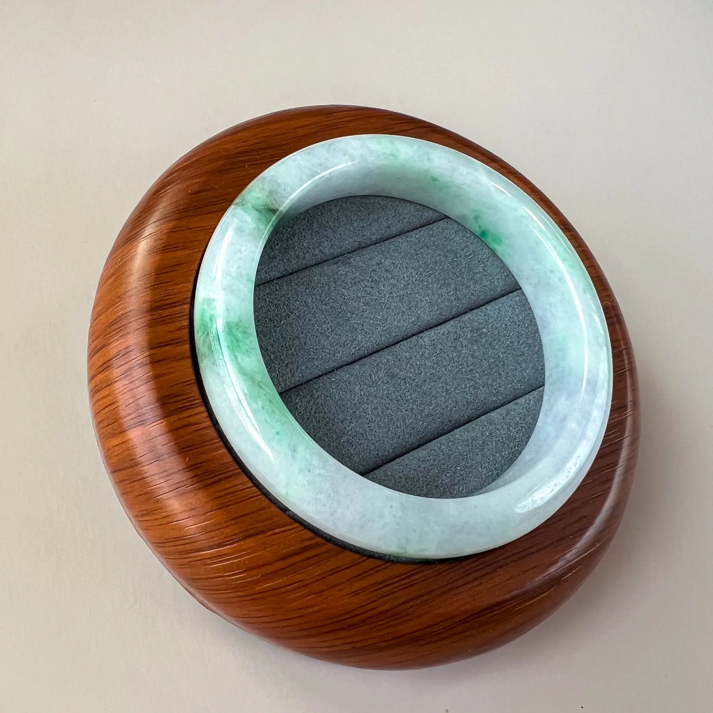 Angled view of pale green and white jade bangle on wood display base