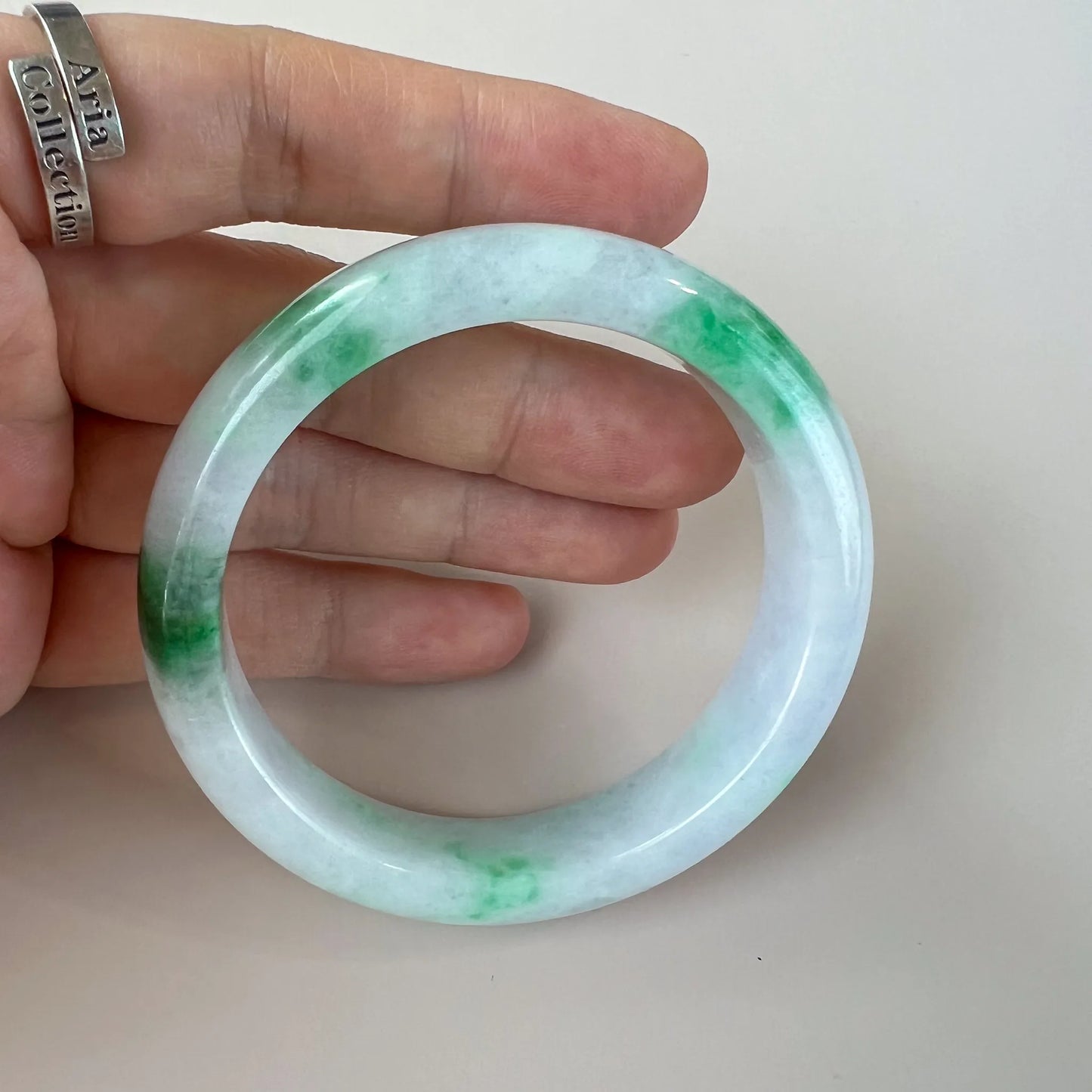Handheld view of translucent jade bangle with green veining and glossy polish