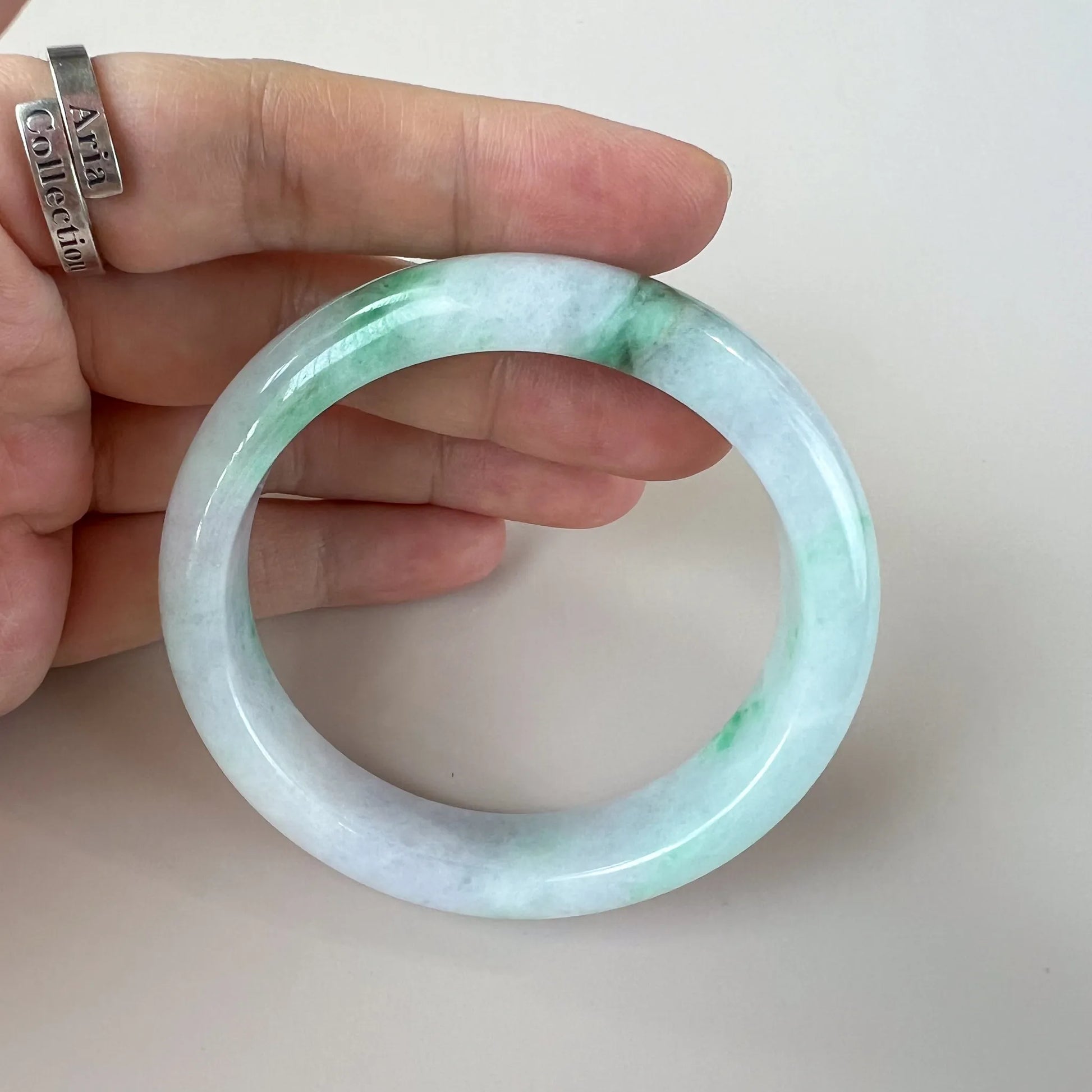 Handheld view of smooth jade bangle, pale green and white tones with polished surface