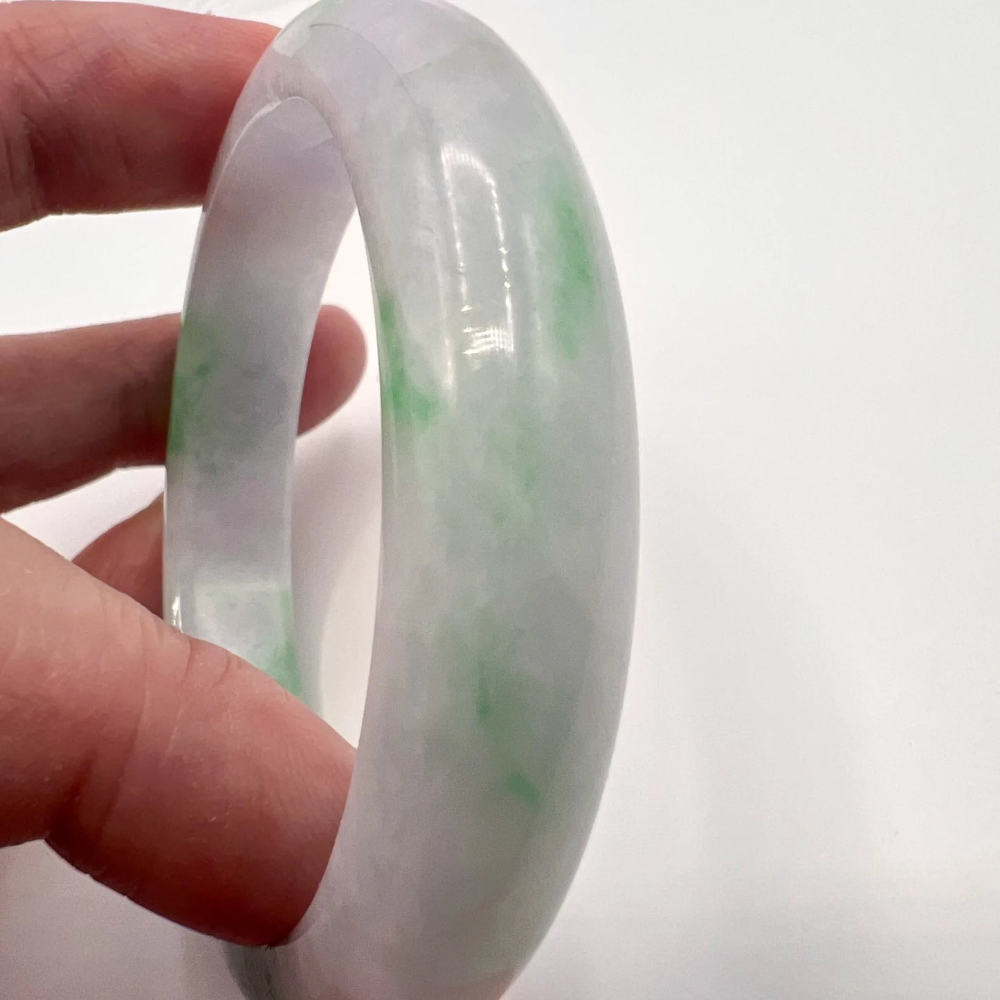 A hand holding a translucent white jade bangle with green mottled inclusions against a plain white background.