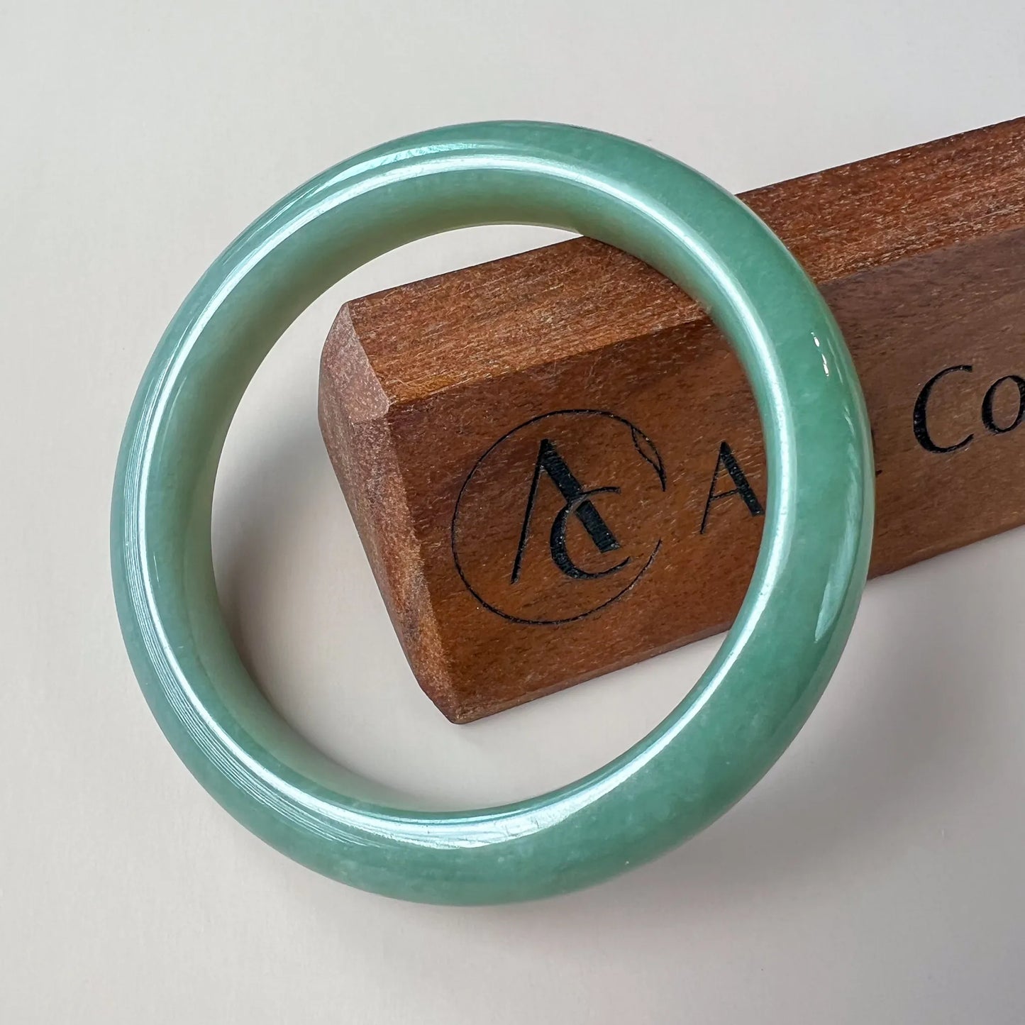 Front view of glossy green jade bangle on white background with wooden display block