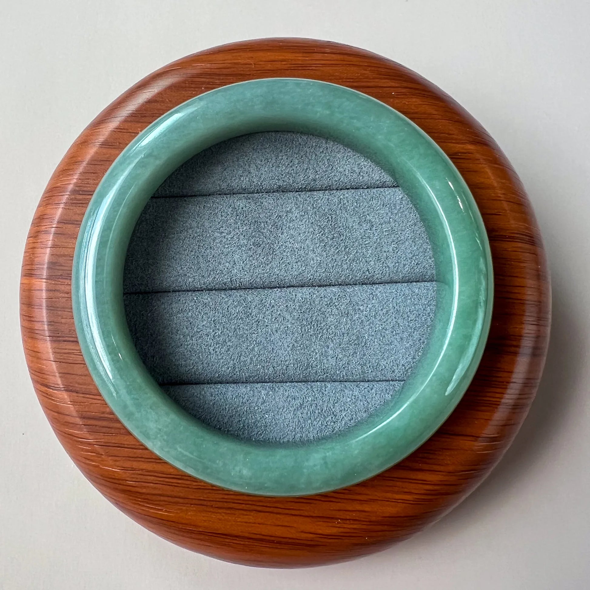 Top-down view of polished green jade bangle resting on round wooden stand