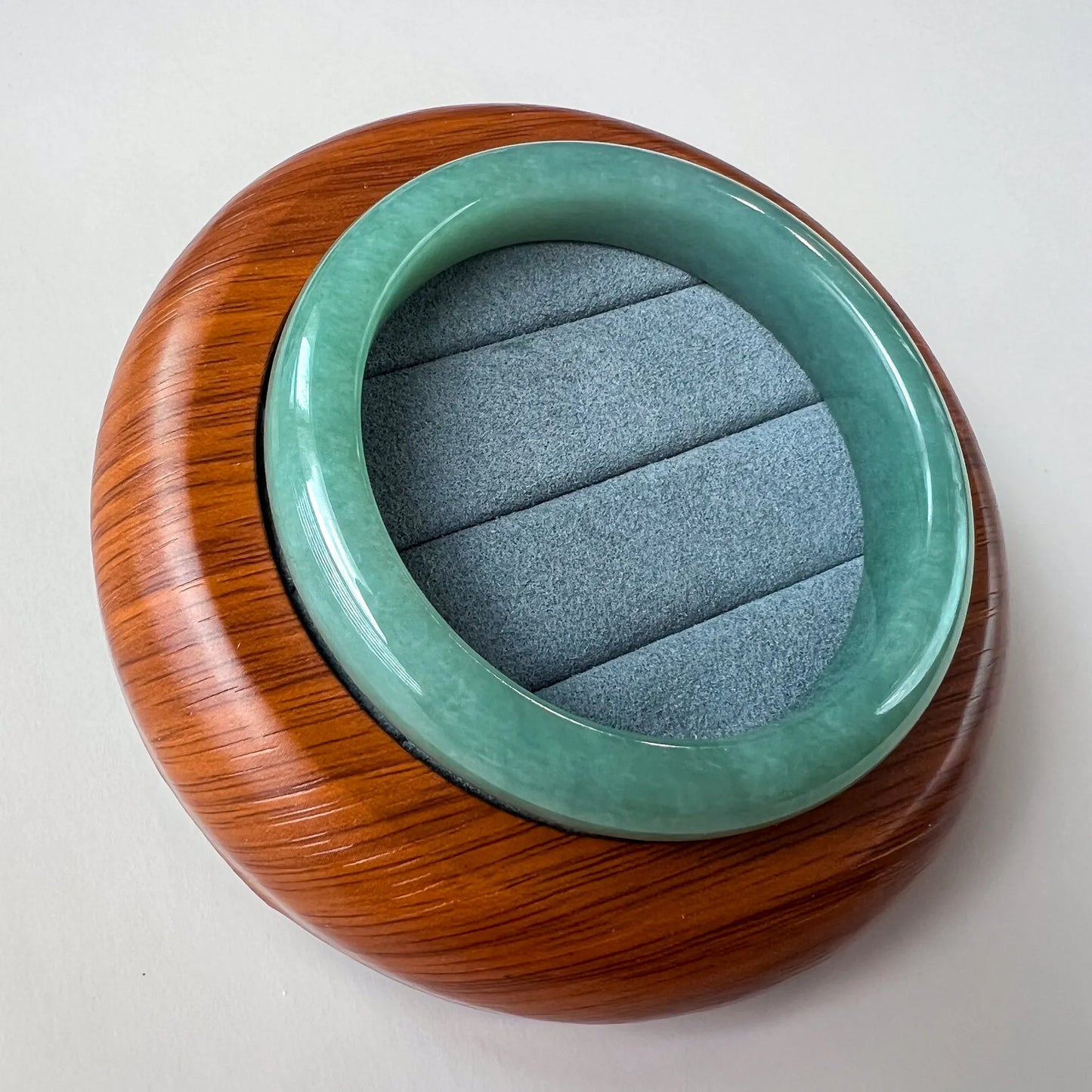 Angled view of glossy green jade bangle on wood display base with gray cushion