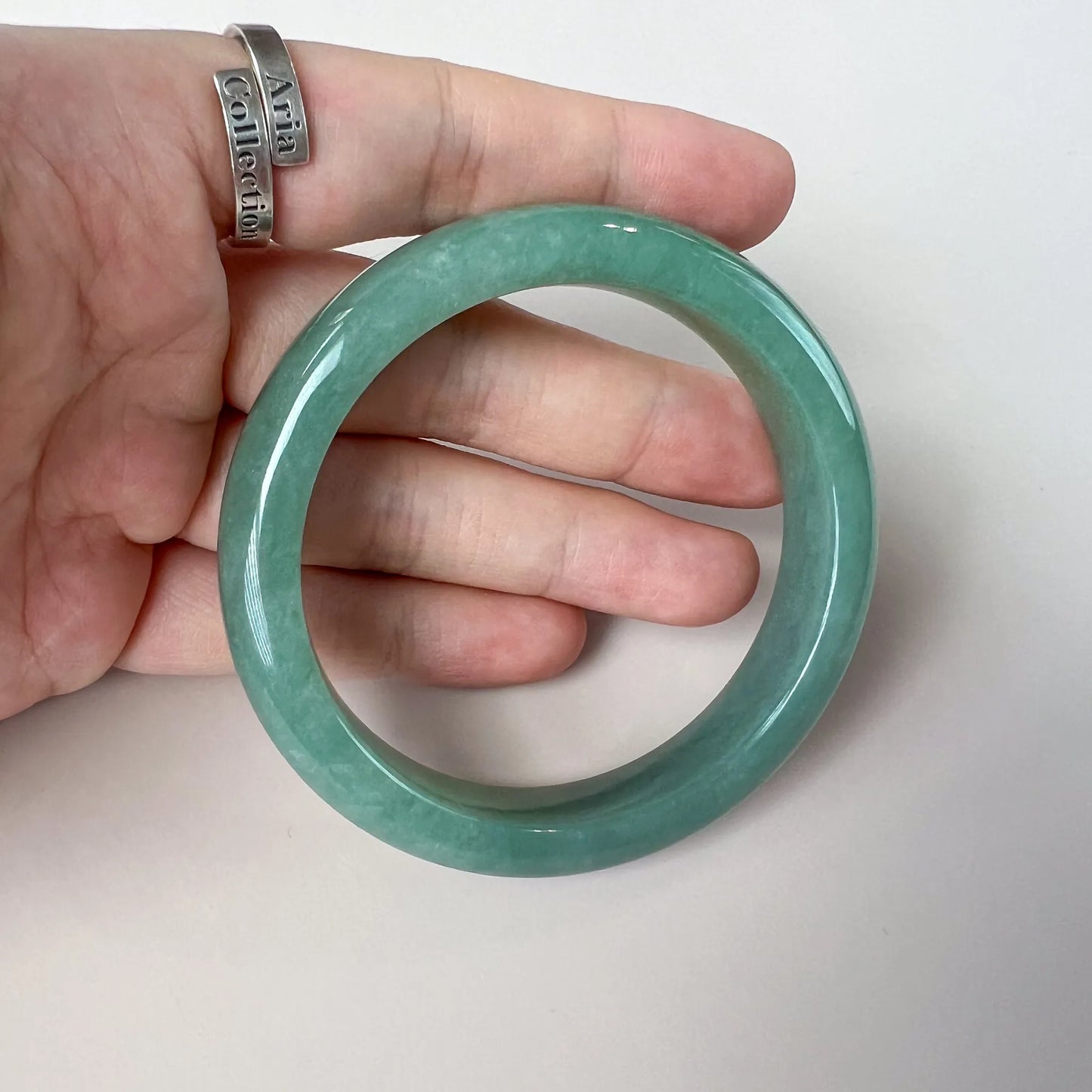 Handheld close-up of glossy green jade bangle with smooth round profile