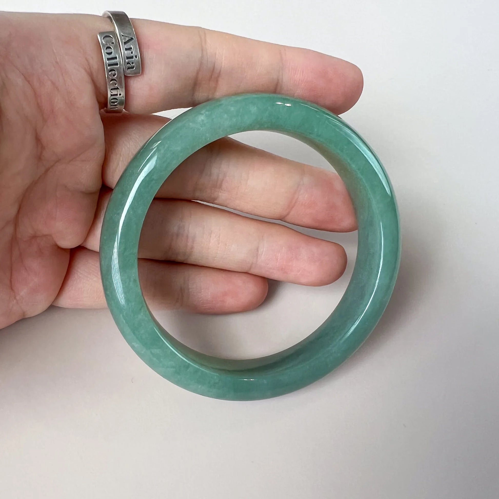 Handheld close-up of glossy green jade bangle with smooth round profile