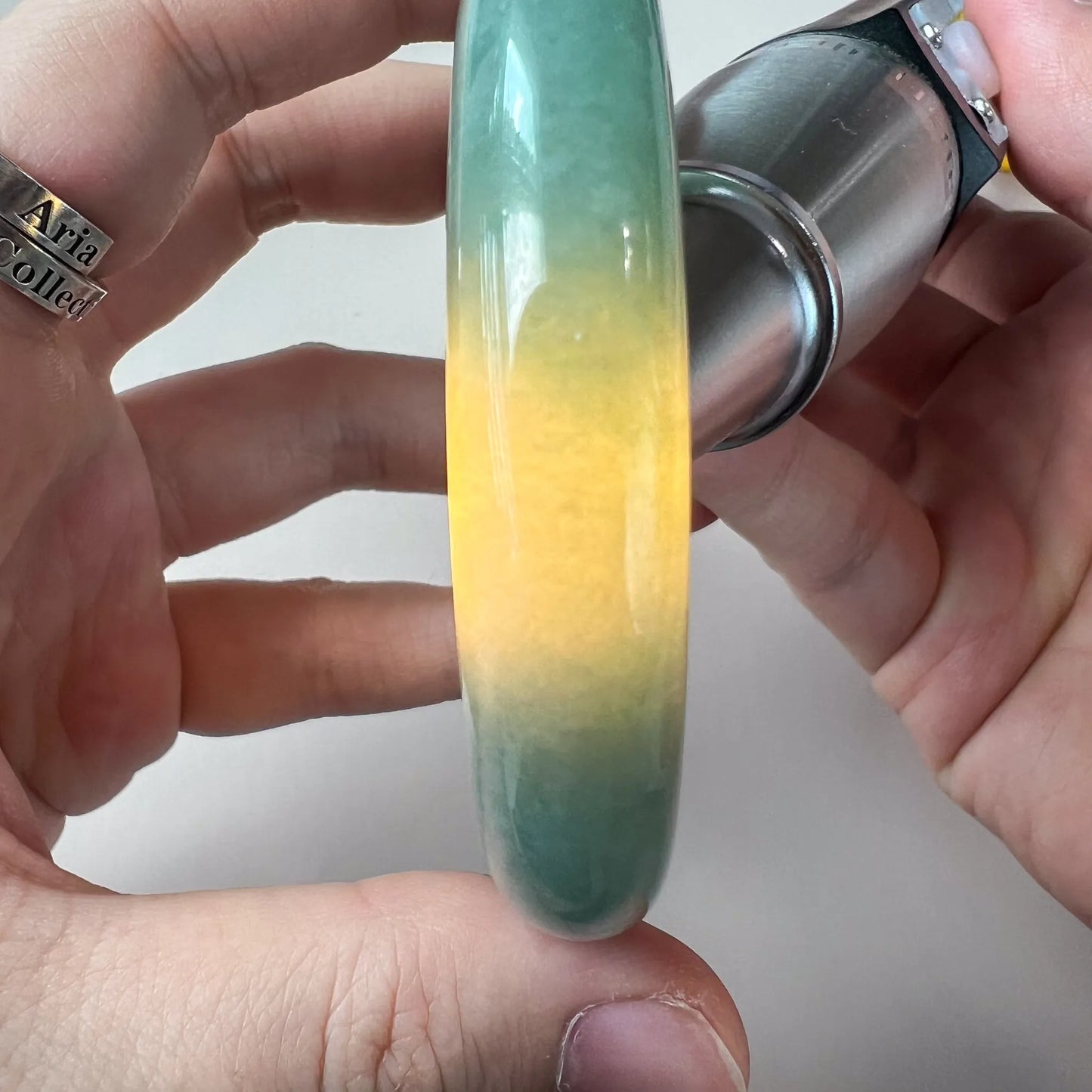 Side view of jade bangle with vivid yellow center and green edges under spotlight