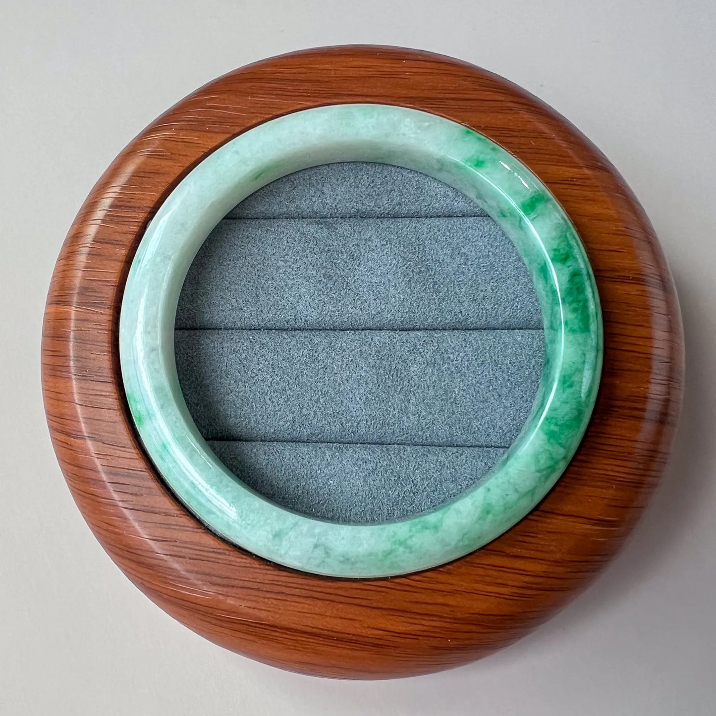 jade bangle resting on wooden display case, top view with smooth polished finish