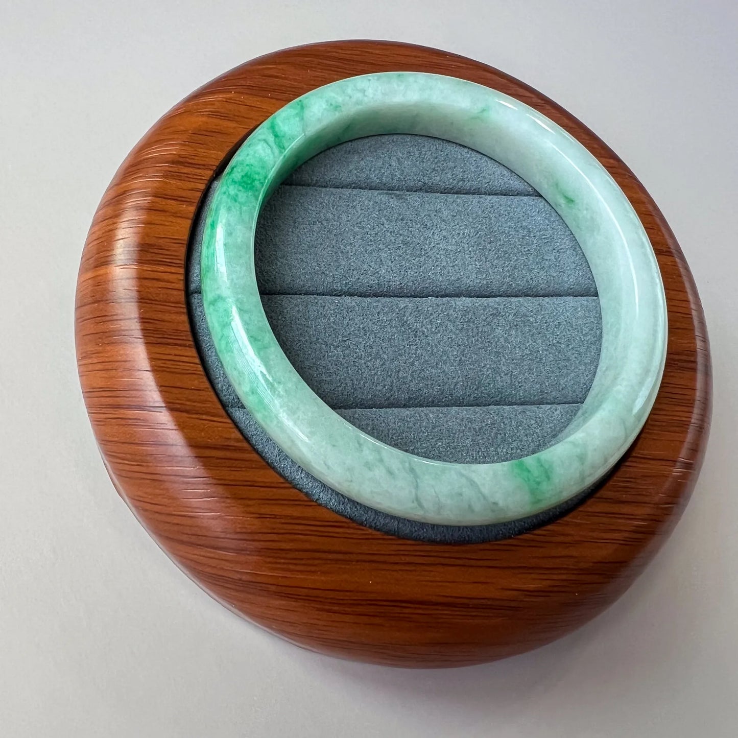 green jade bangle on wood stand, angled view showing glossy round profile