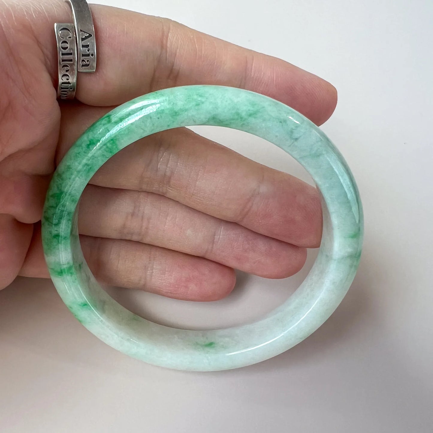 handheld view of mottled green jade bangle, polished stone finish and round shape