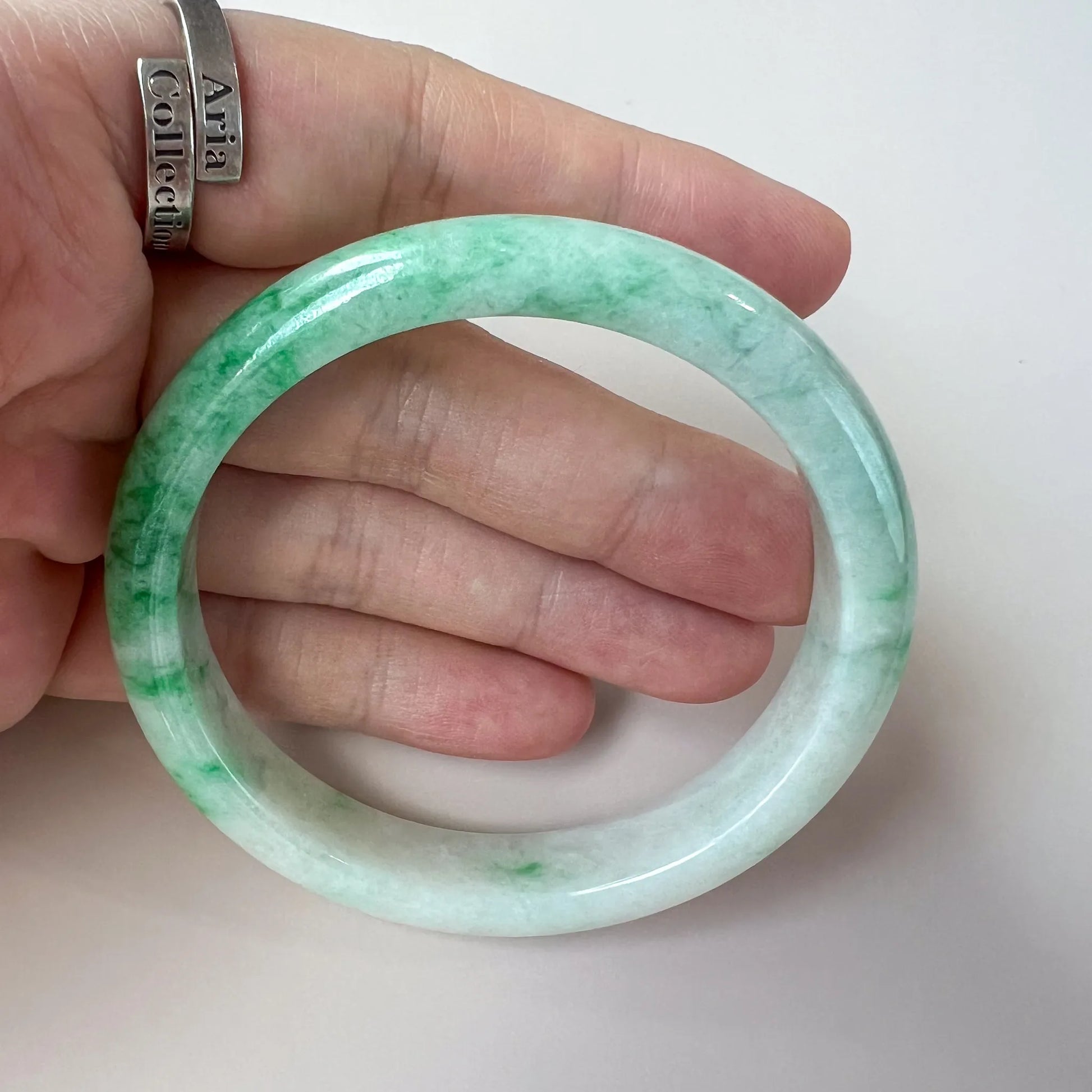 handheld view of mottled green jade bangle, polished stone finish and round shape