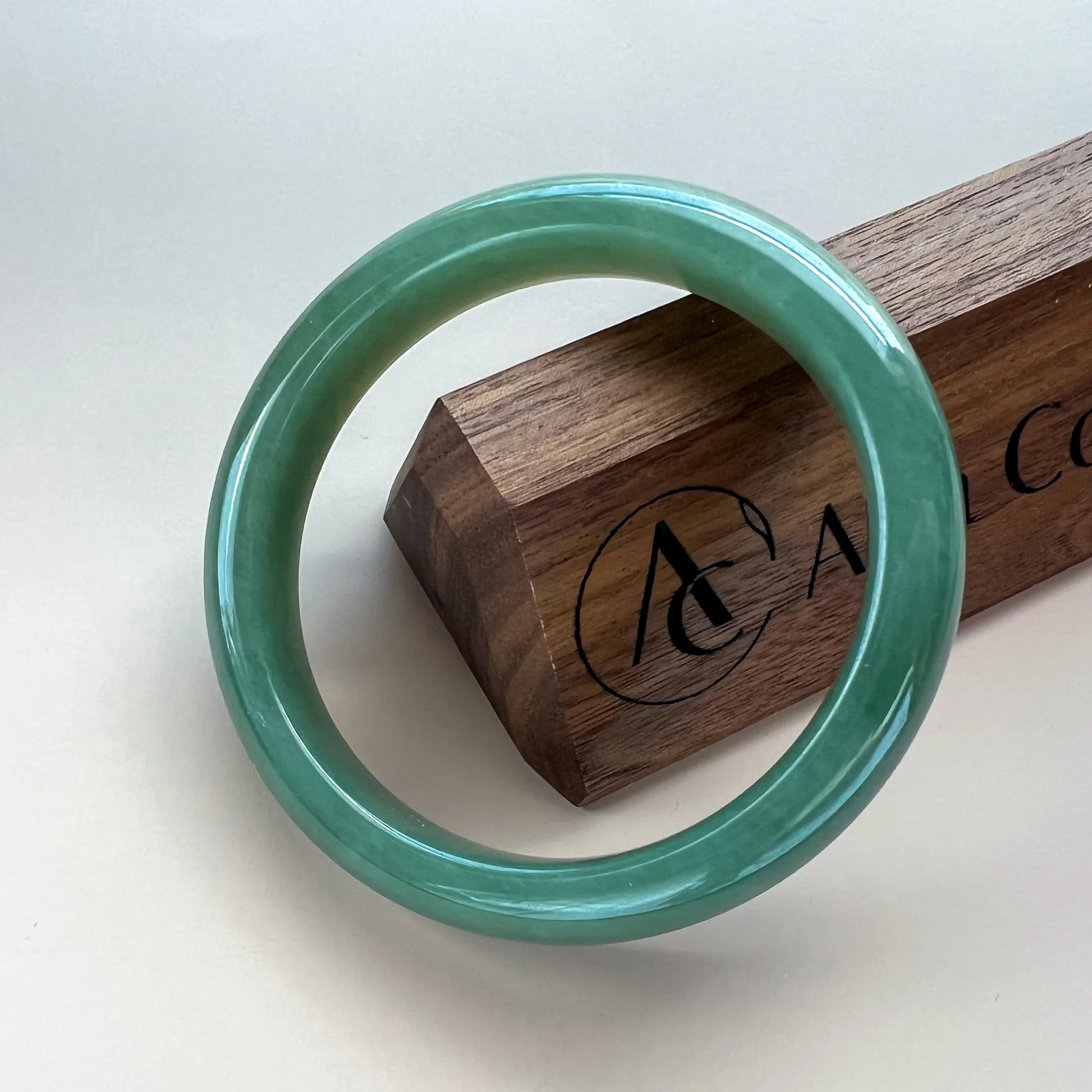 Front view of polished green jade bangle on wood display, glossy round profile