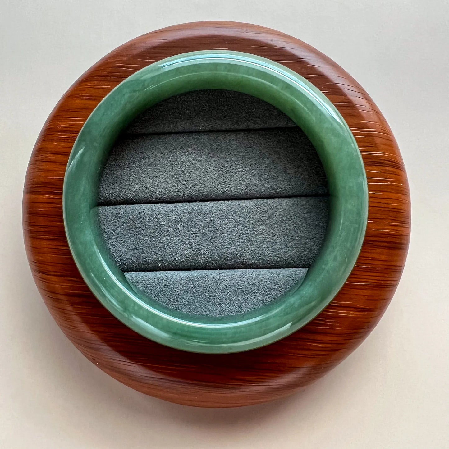 Top view of green jade bangle in round wooden case with suede lining