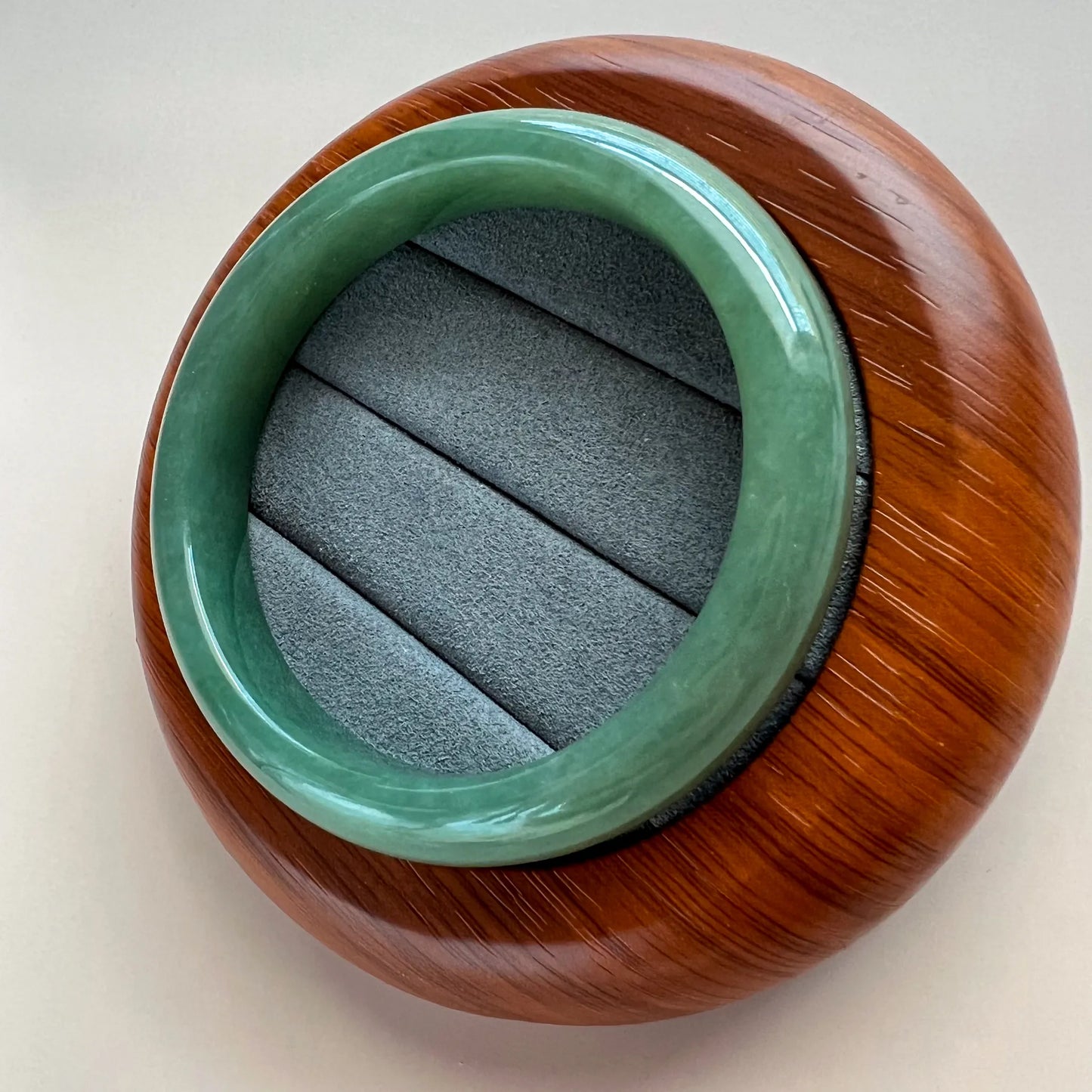 Angled view of polished green jade bangle in fitted wooden display case