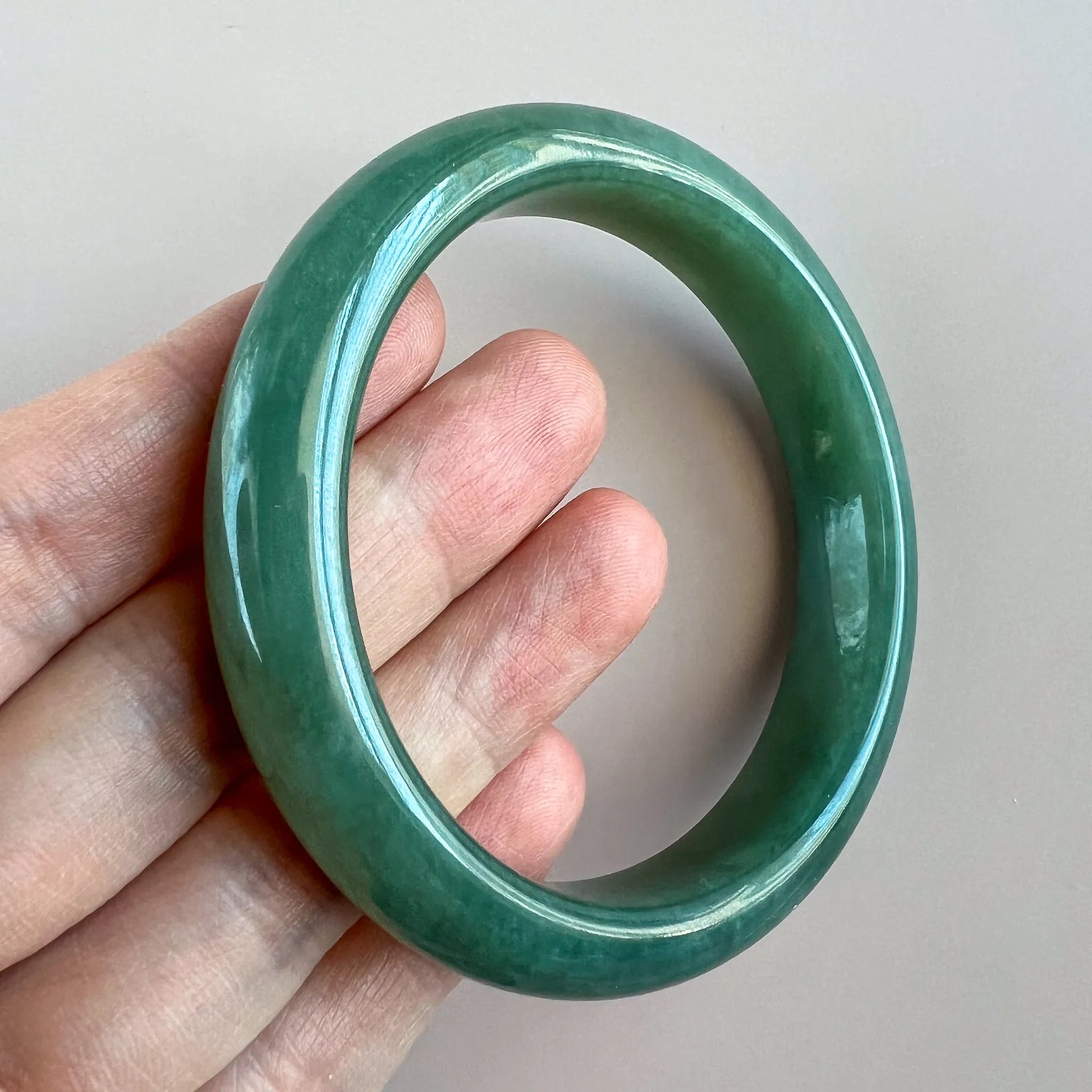 Three-quarter view of green jade bangle held in hand, glossy translucent finish