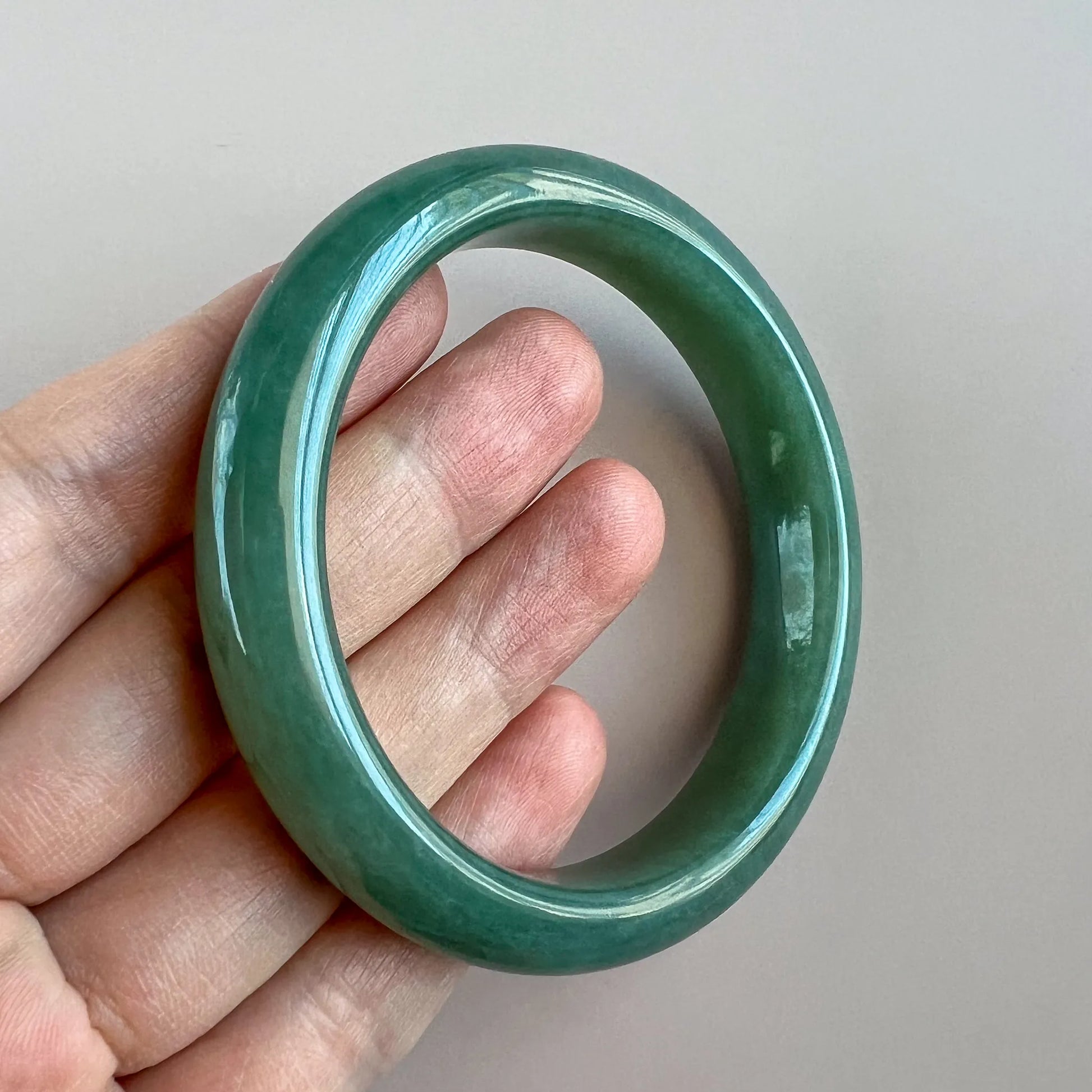 Angled view of green jade bangle held in hand, smooth polished stone