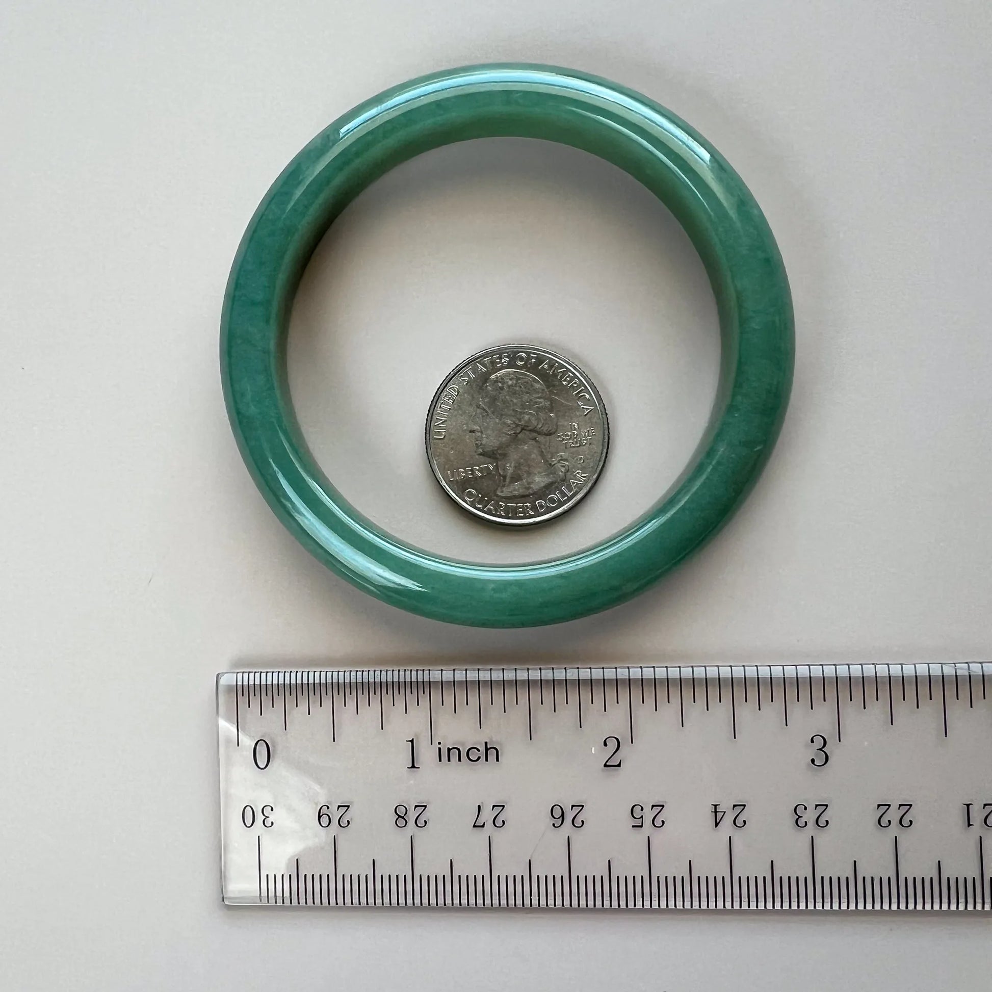 Green jadeite bangle shown face-on beside a quarter and ruler for scale
