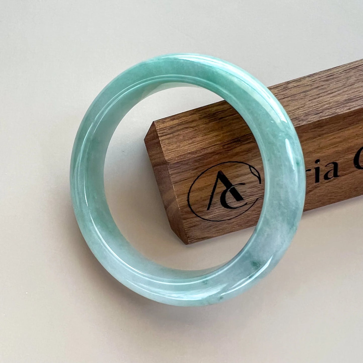 Front view of a pale aqua jade bangle with glossy polish, shown against a wooden display block.
