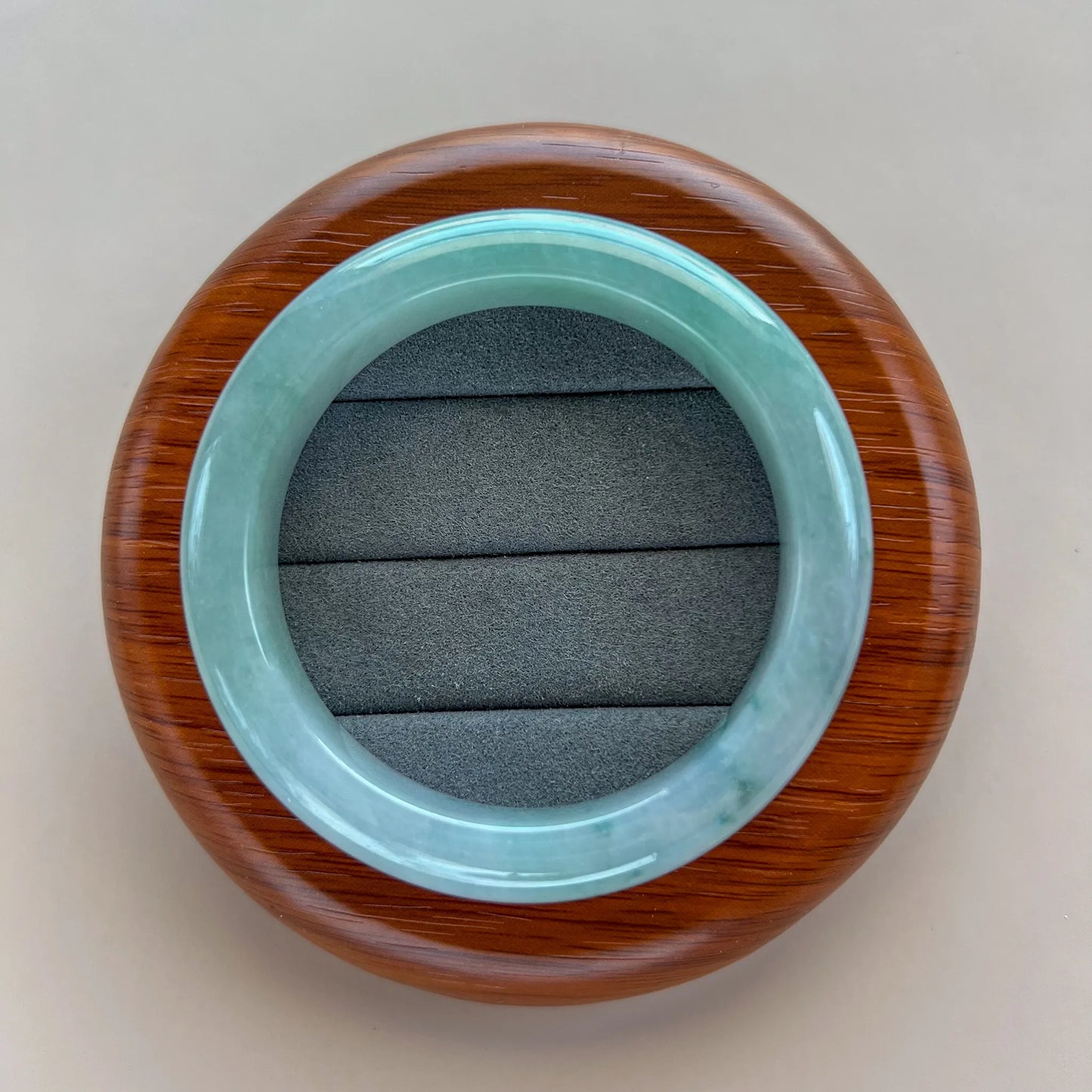 Top view of light green jade bangle on a round wood display stand with gray cushion insert.