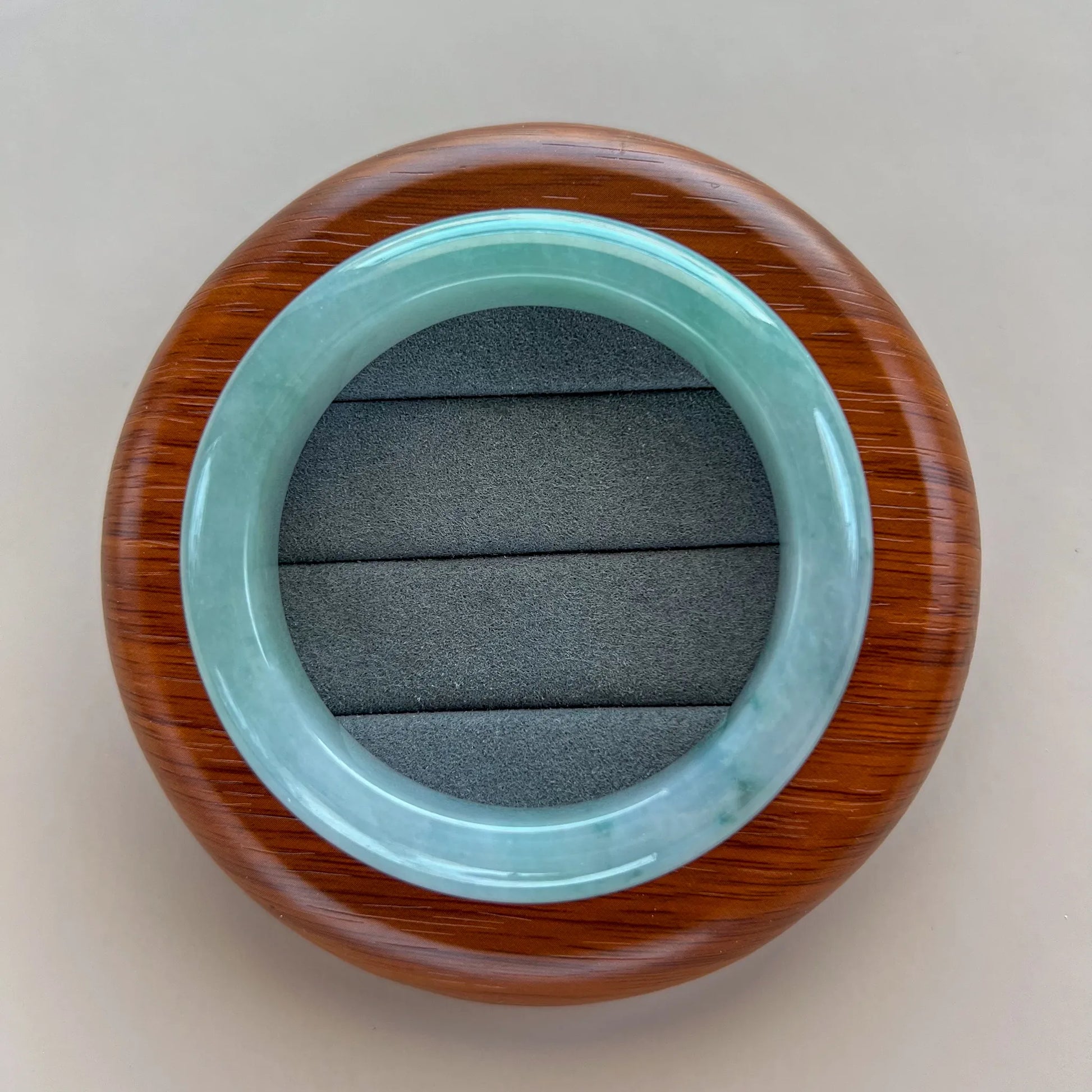 Top view of light green jade bangle on a round wood display stand with gray cushion insert.